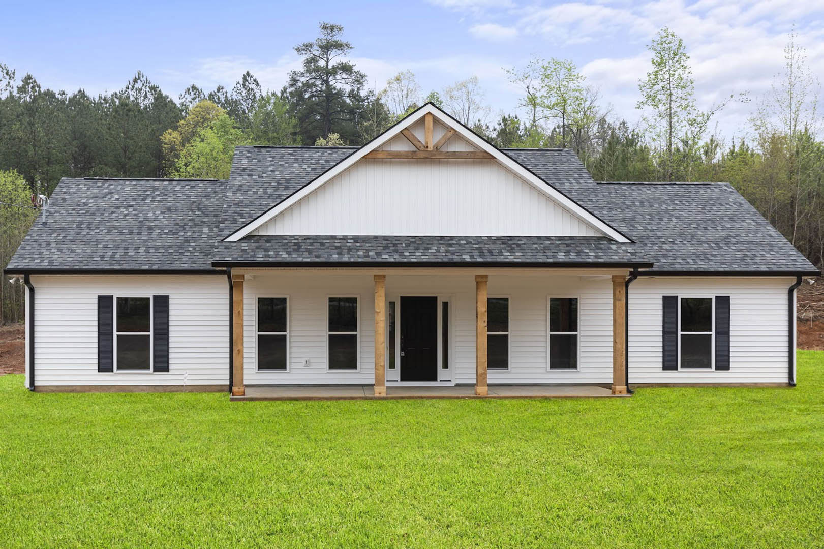 White house with black door and white trim, front lawn, white columns, windows with white frames, cloudy sky in background.