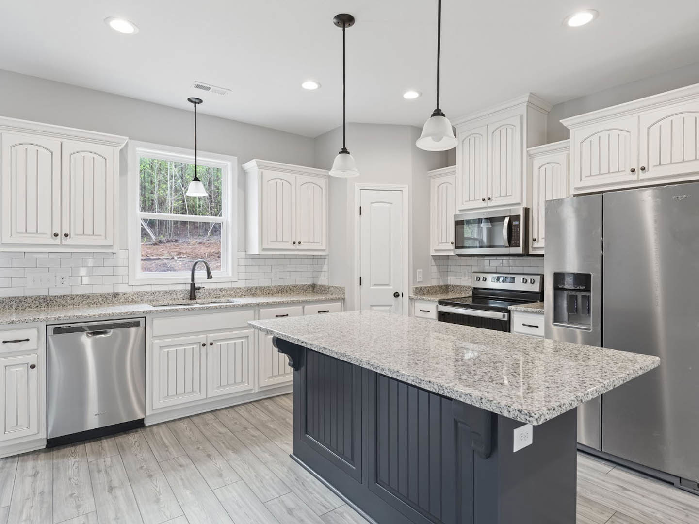 White kitchen cabinets, granite island countertop, stainless steel microwave with glass door, close-up of dishwasher, refrigerator adjacent to granite counter, kitchen island with