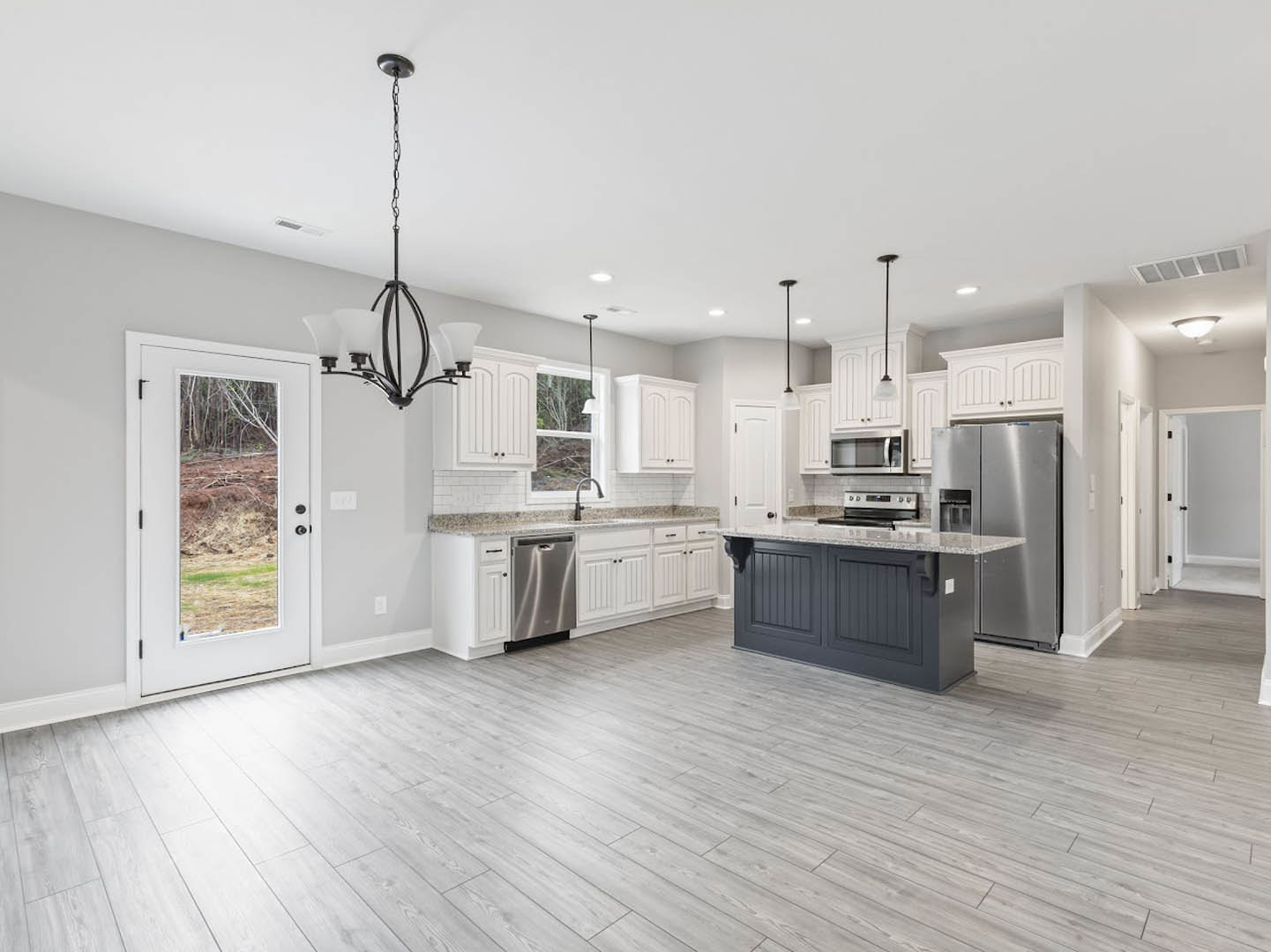 Modern kitchen with marble island countertop, stainless steel refrigerator, white cabinetry, tile backsplash, built-in microwave, and door opening to forest view