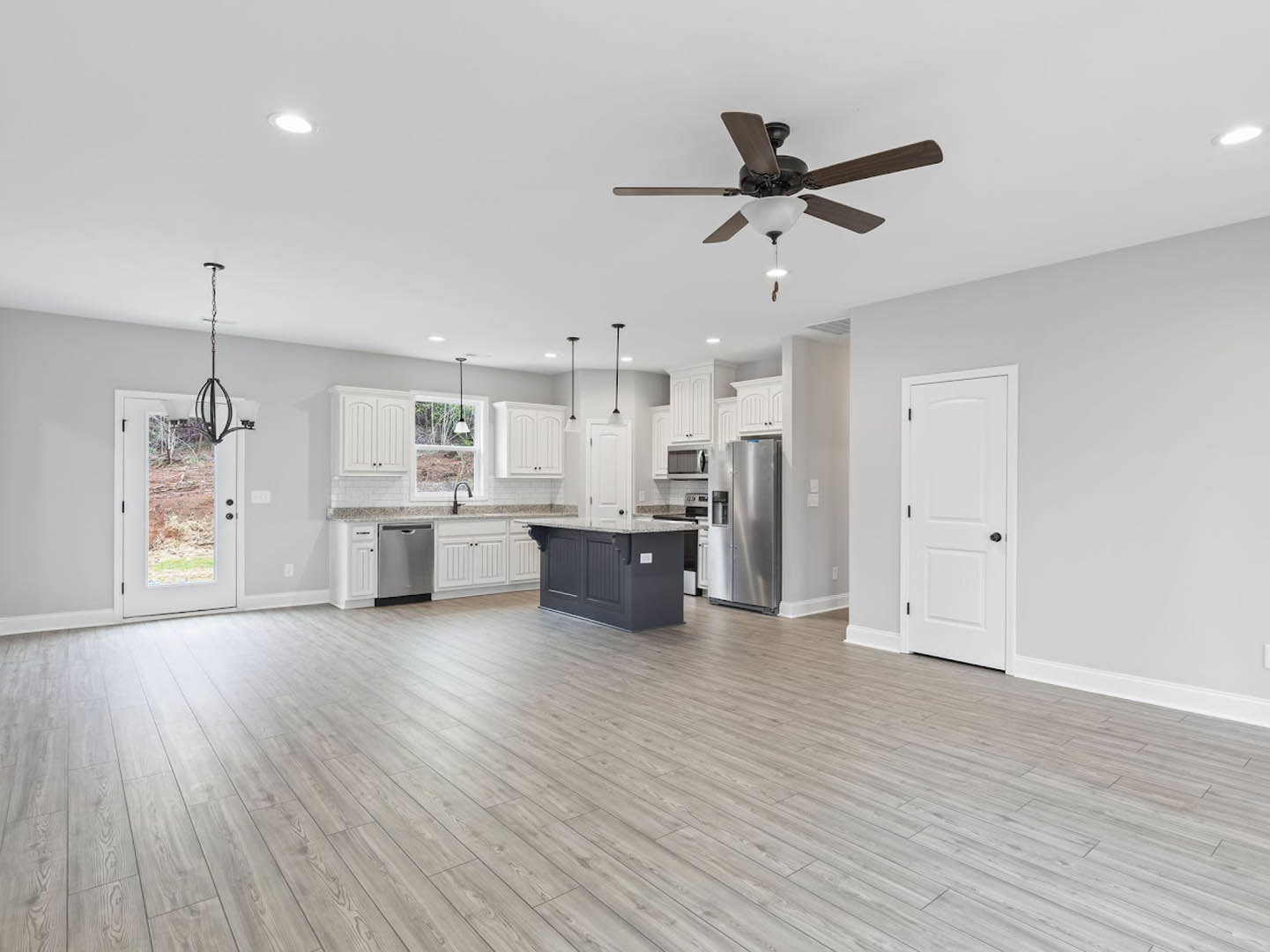 Open-concept kitchen and living room with wood flooring, marble-topped island, white cabinetry, ceiling fan with light fixture, black and silver doors, and black hardware on white