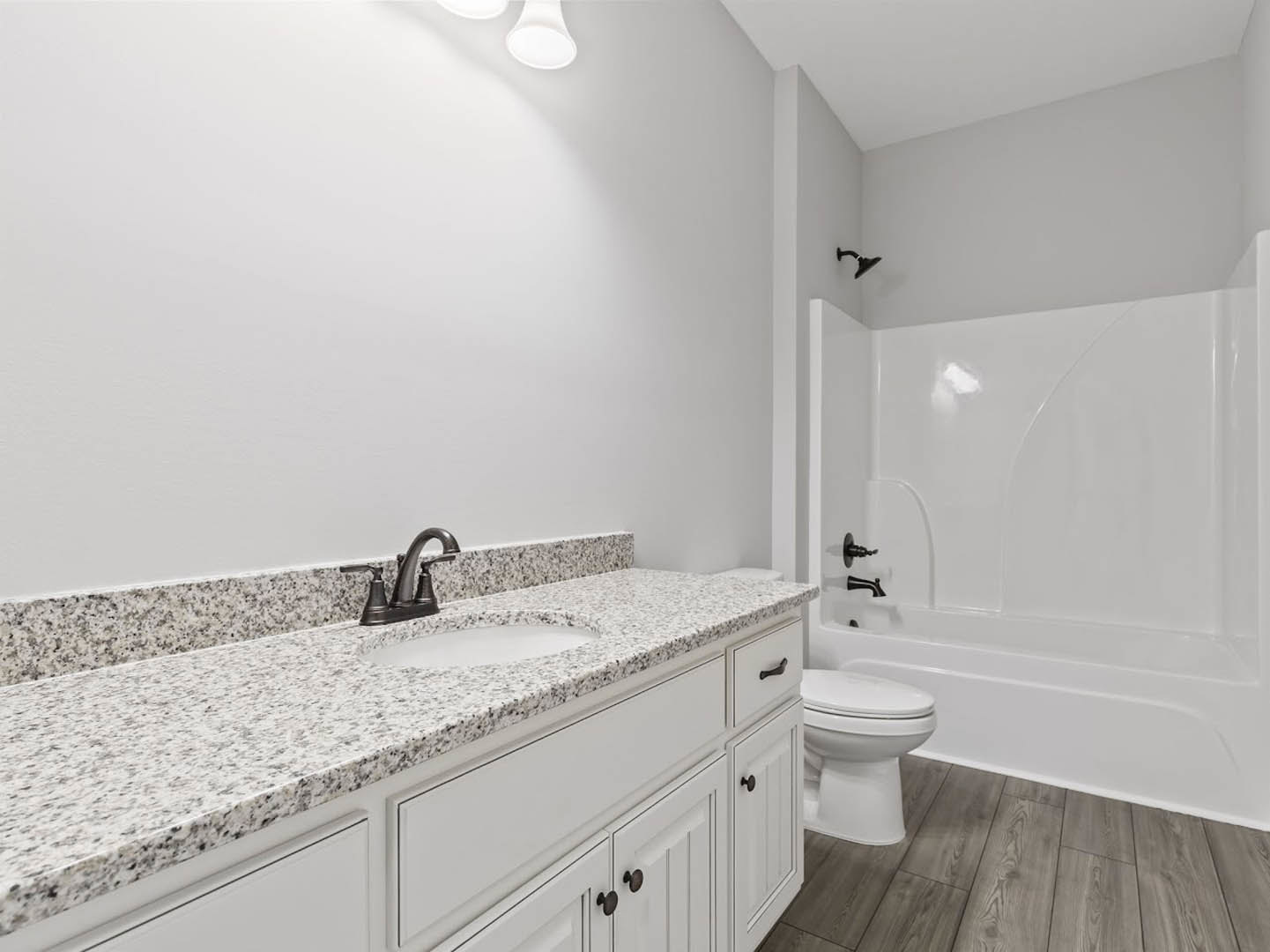 Modern bathroom with white tile walls, a white toilet, rectangular sink set in a wood vanity, black faucet fixtures, and a glass-enclosed shower