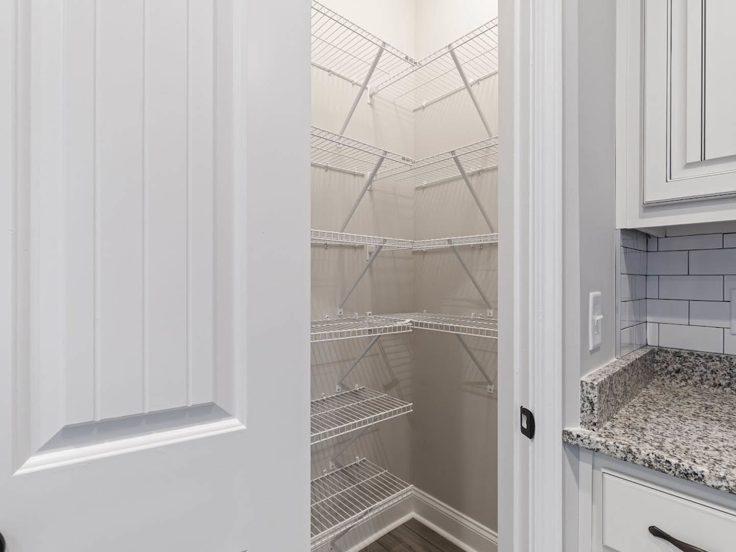 Walk-in closet featuring built-in white shelves, white cabinetry, and a closed white door, with smooth countertop and drawer details visible.