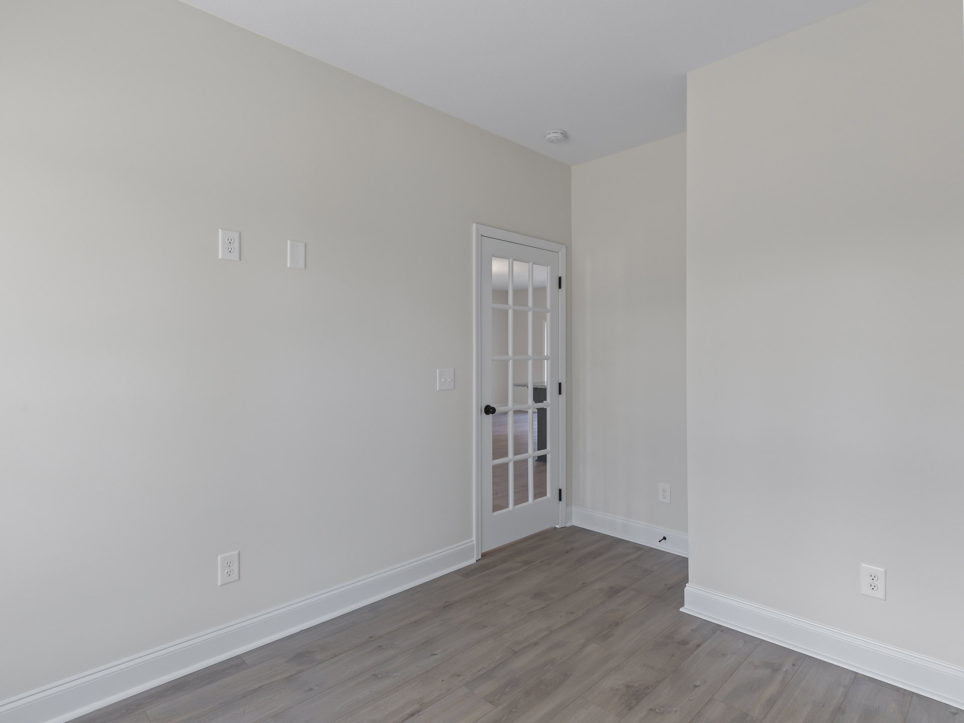 White room with wood flooring, white walls, glass-paneled door, window, and white baseboard molding