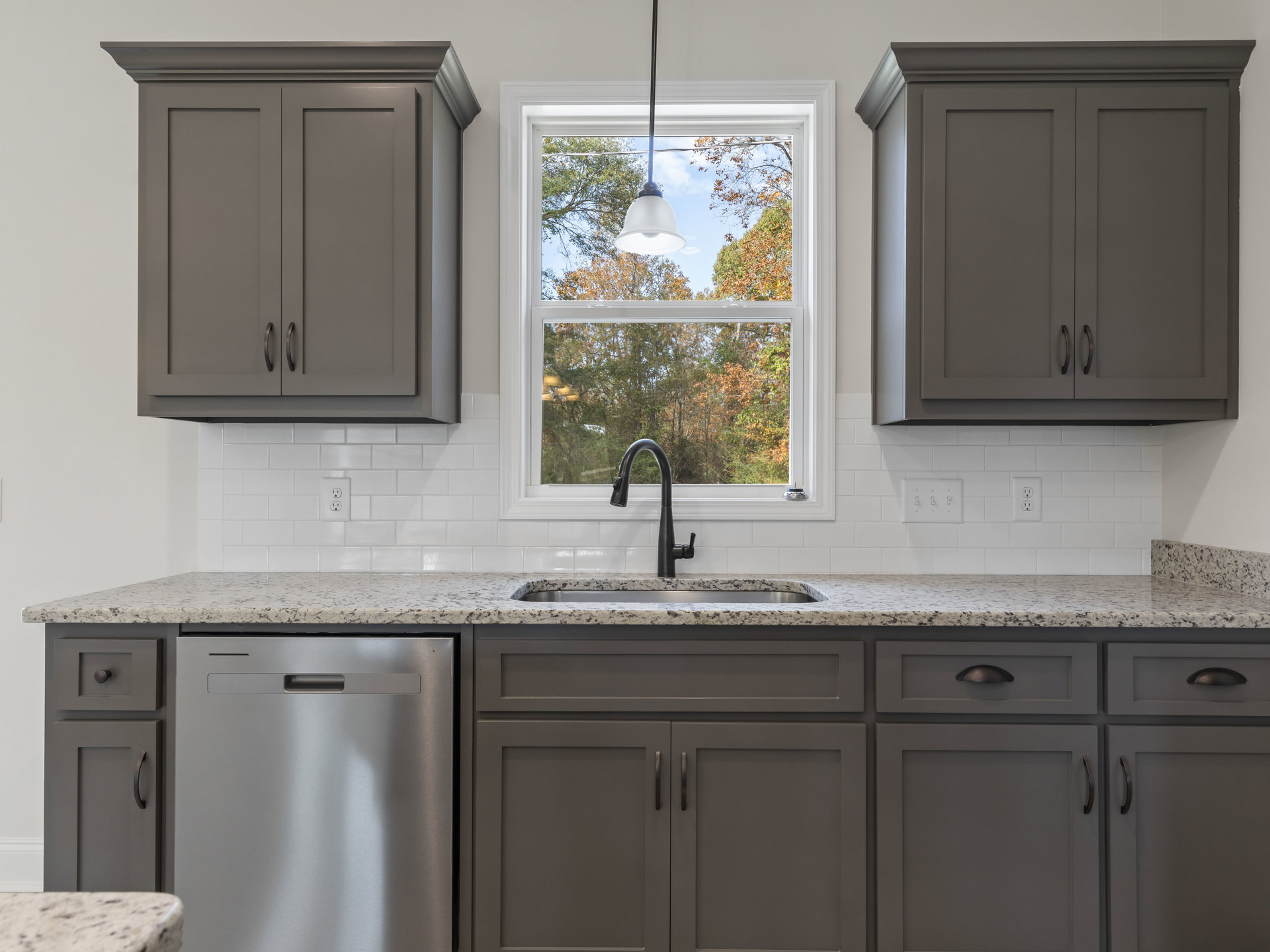Bright kitchen featuring white cabinetry, stainless steel dishwasher with handle, undermount sink and chrome faucet set in light stone countertop, large window above sink revealing