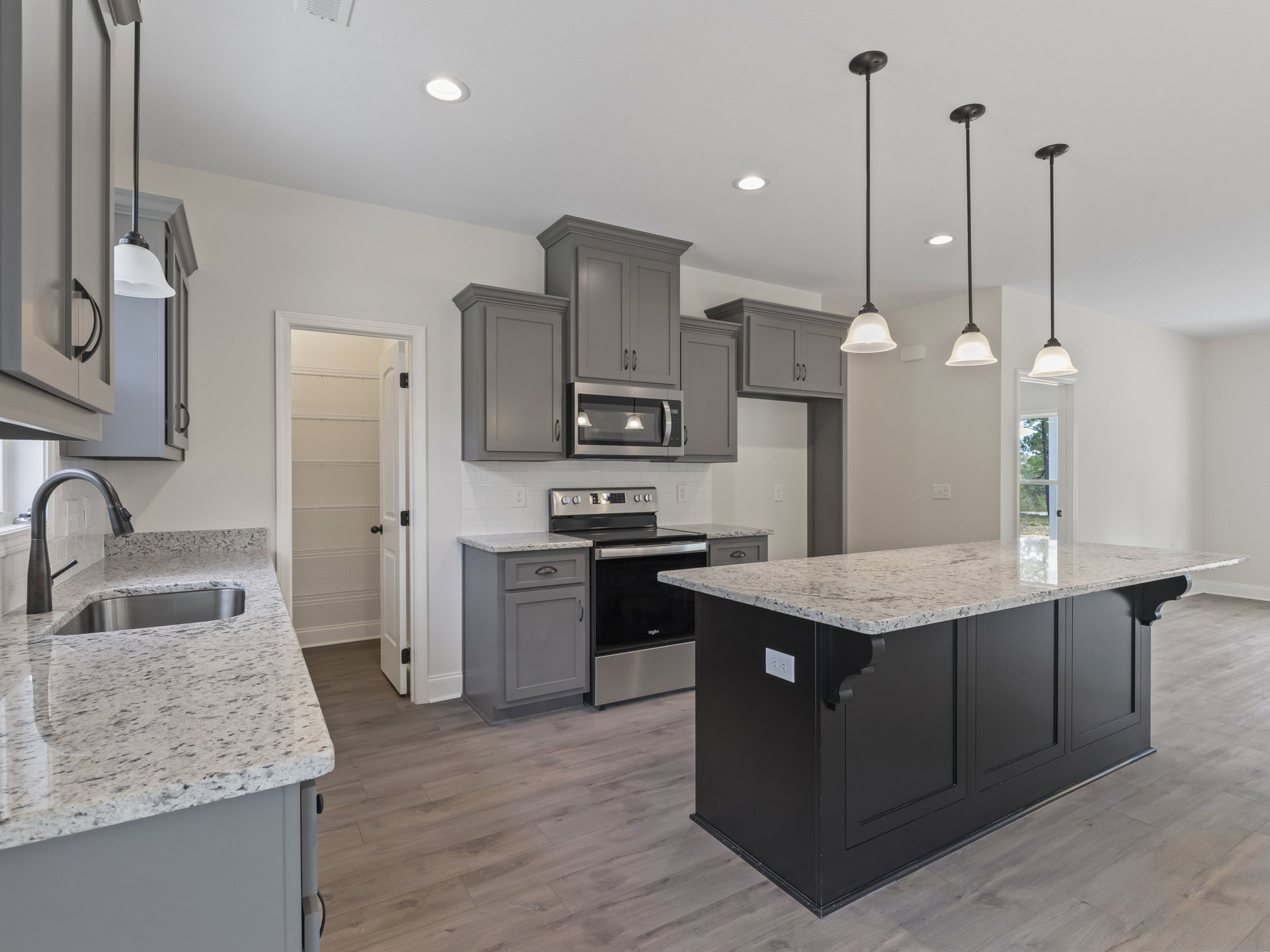 Spacious kitchen featuring a marble-topped island, stainless steel stove and oven, tile backsplash, white cabinetry, built-in microwave, and pendant ceiling light