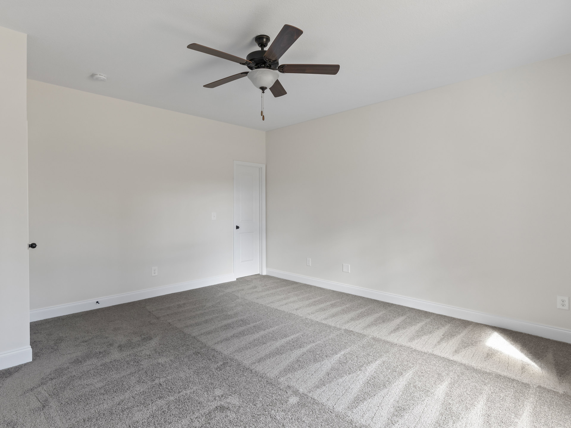 Carpeted room with white walls, white door featuring a black knob, ceiling fan with light fixture mounted on plaster ceiling