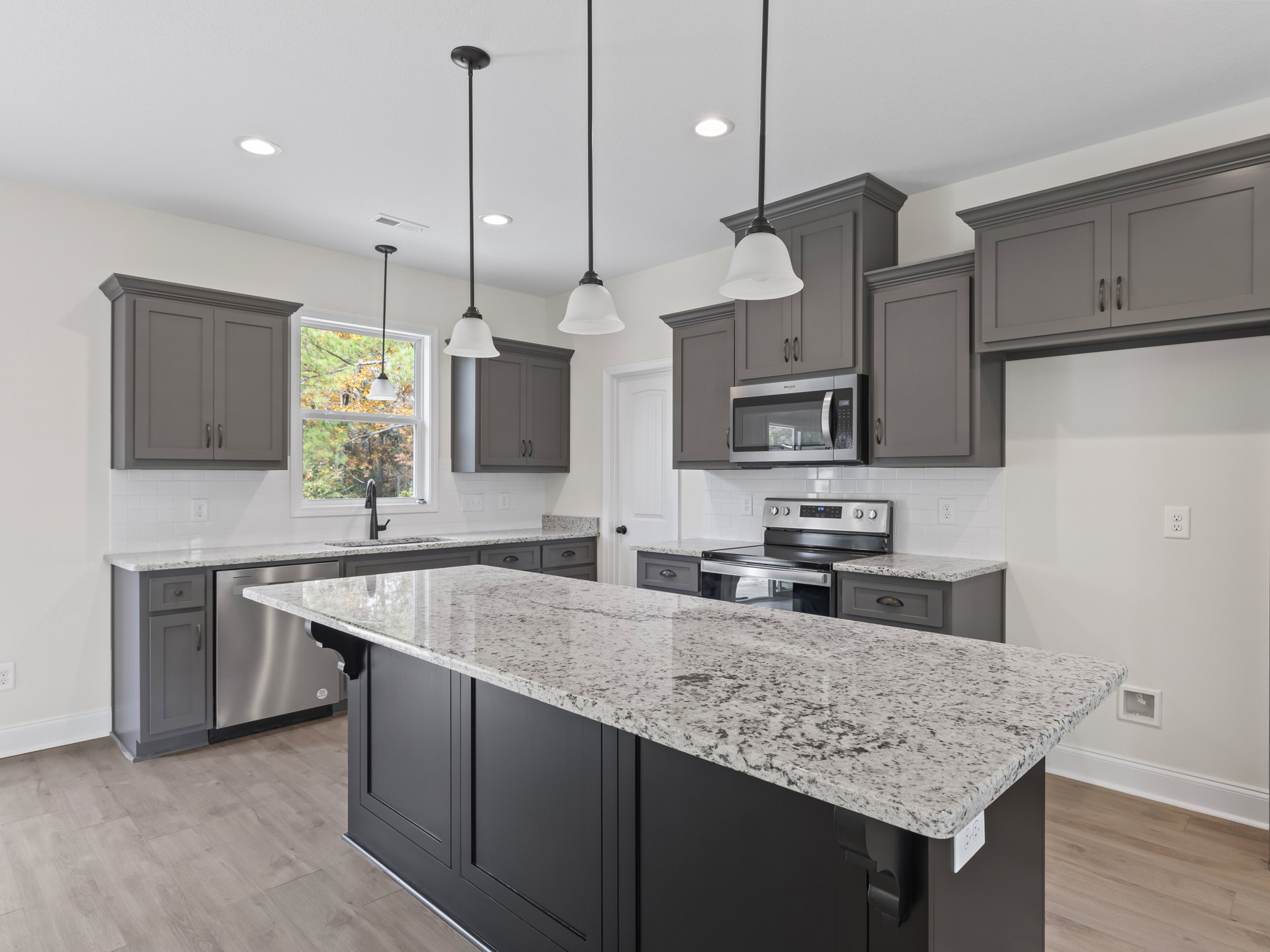 Marble island with waterfall edge, white cabinetry, stainless steel microwave, granite countertops, pendant light fixture, sunlight streaming through window, undermount sink