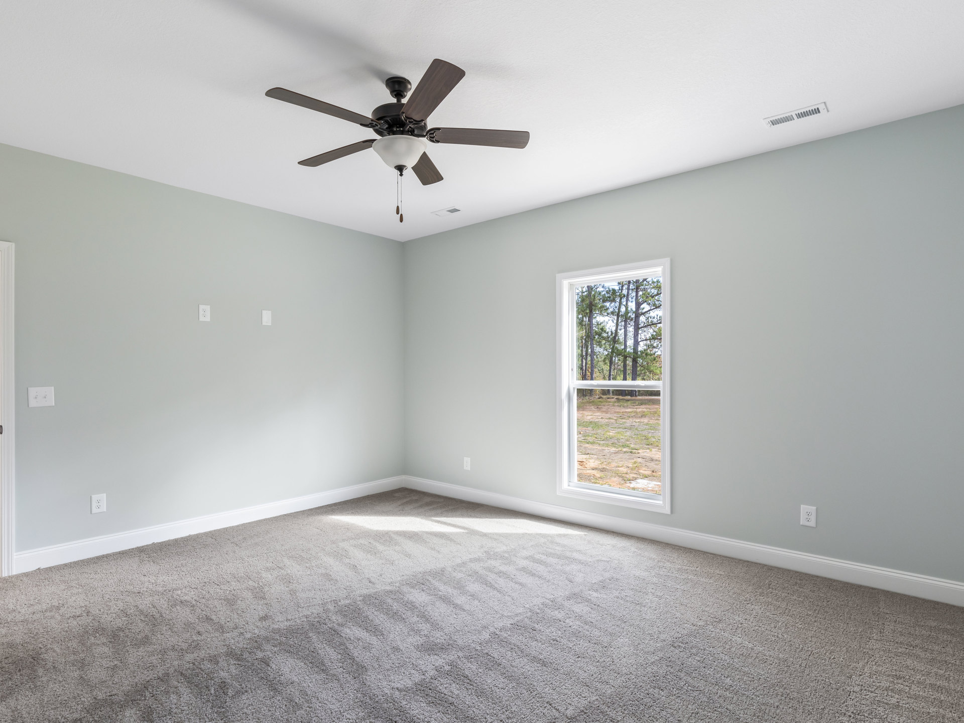 Carpeted bedroom with white walls, ceiling fan with light fixture, large window overlooking grassy field and trees