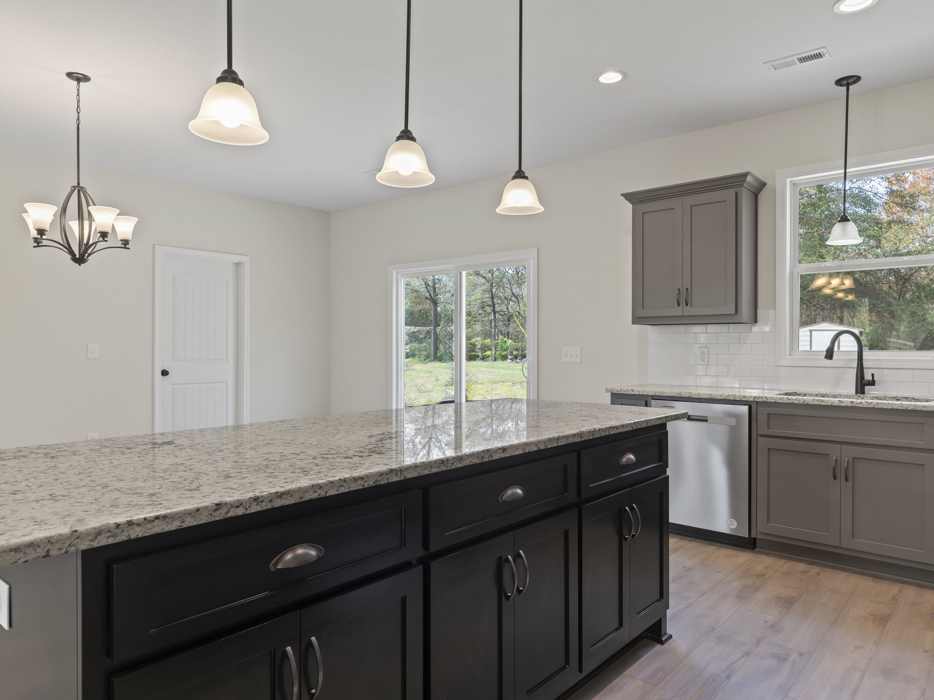 Spacious kitchen featuring a large central island with grey cabinetry and handles, white door with black knob, multiple ceiling light fixtures including a chandelier with white