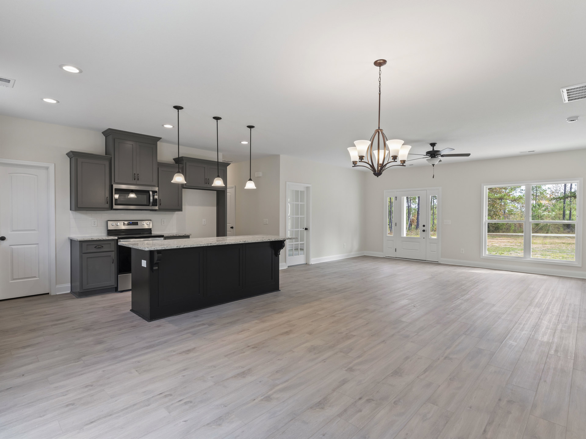 Open kitchen and living room featuring wood flooring, black kitchen island with marble countertops, white cabinetry, stainless steel appliances, white door with black handle, large
