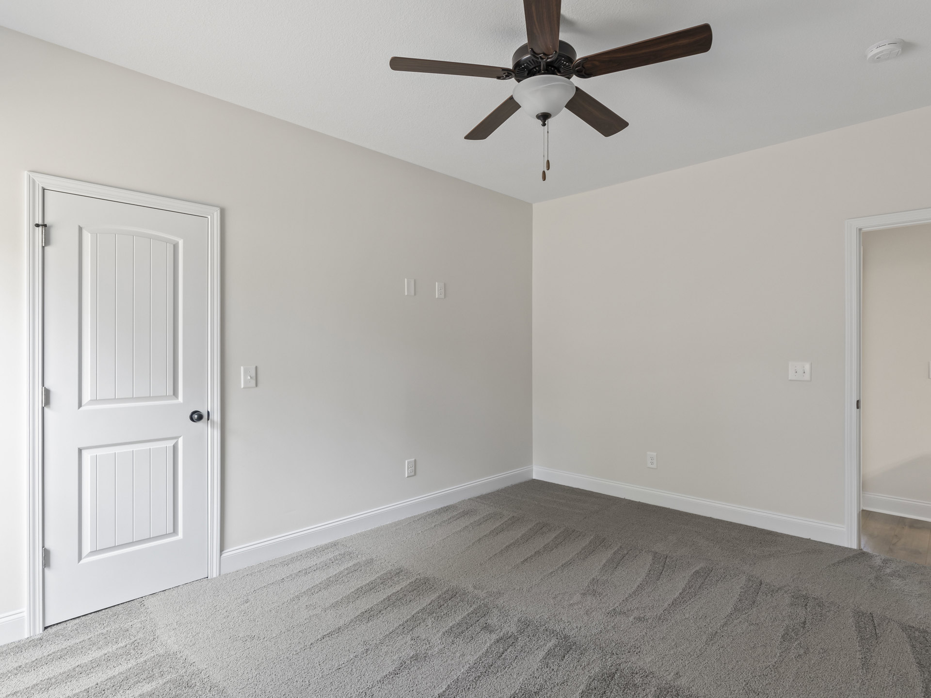 Carpeted room with white paneled door featuring black handle, ceiling fan with light fixture, white walls, and visible light switch