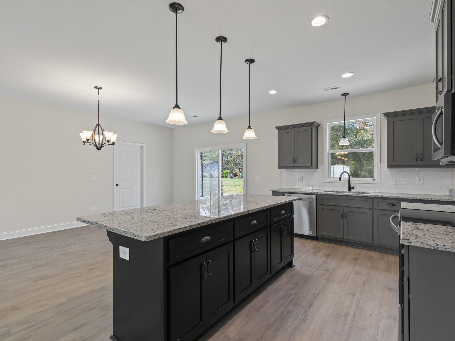 Spacious kitchen featuring a large island with black cabinetry, white quartz countertop, grey cabinets with black handles, stainless steel sink, and a chandelier with white lamps