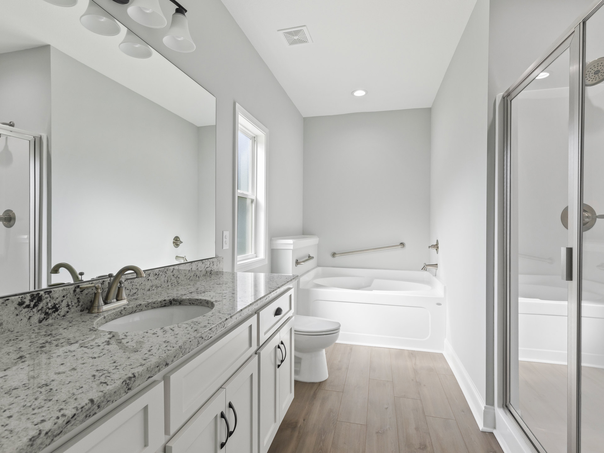 Bathroom featuring marble countertop with undermount sink, freestanding tub, white toilet, white-framed window, black cabinet handle, and light tile flooring.