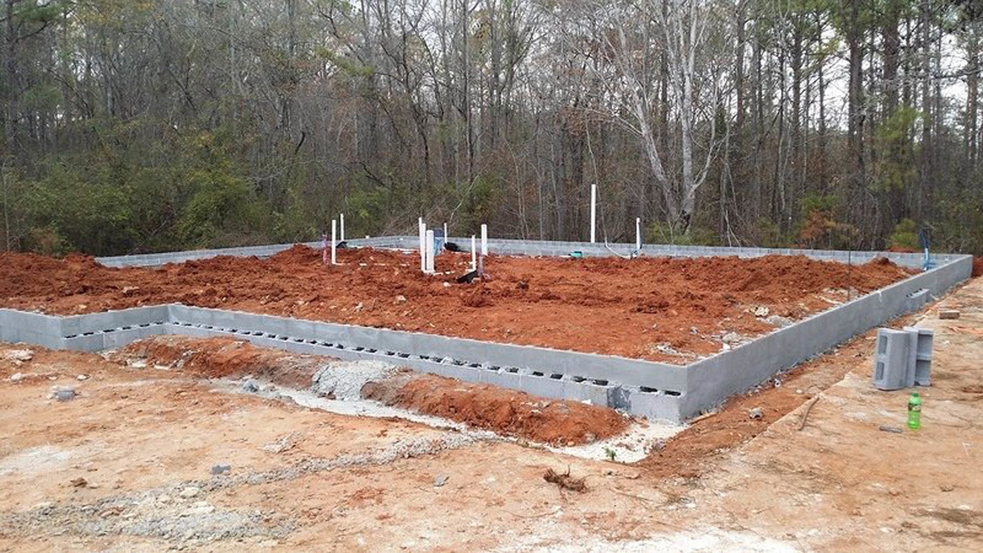 Concrete foundation surrounded by dirt and construction poles, with trees in the background