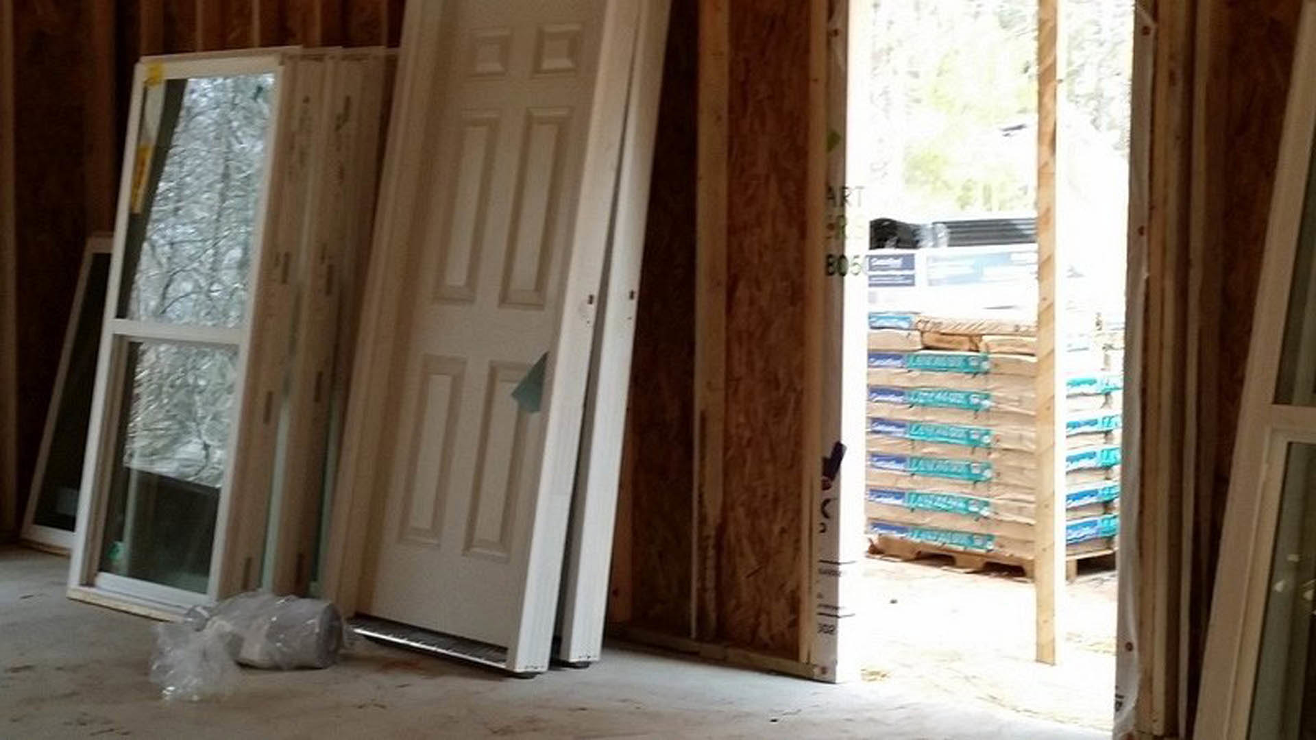 White door with a paper note, glass window, stack of wood pallets and plastic bags in a residential interior room