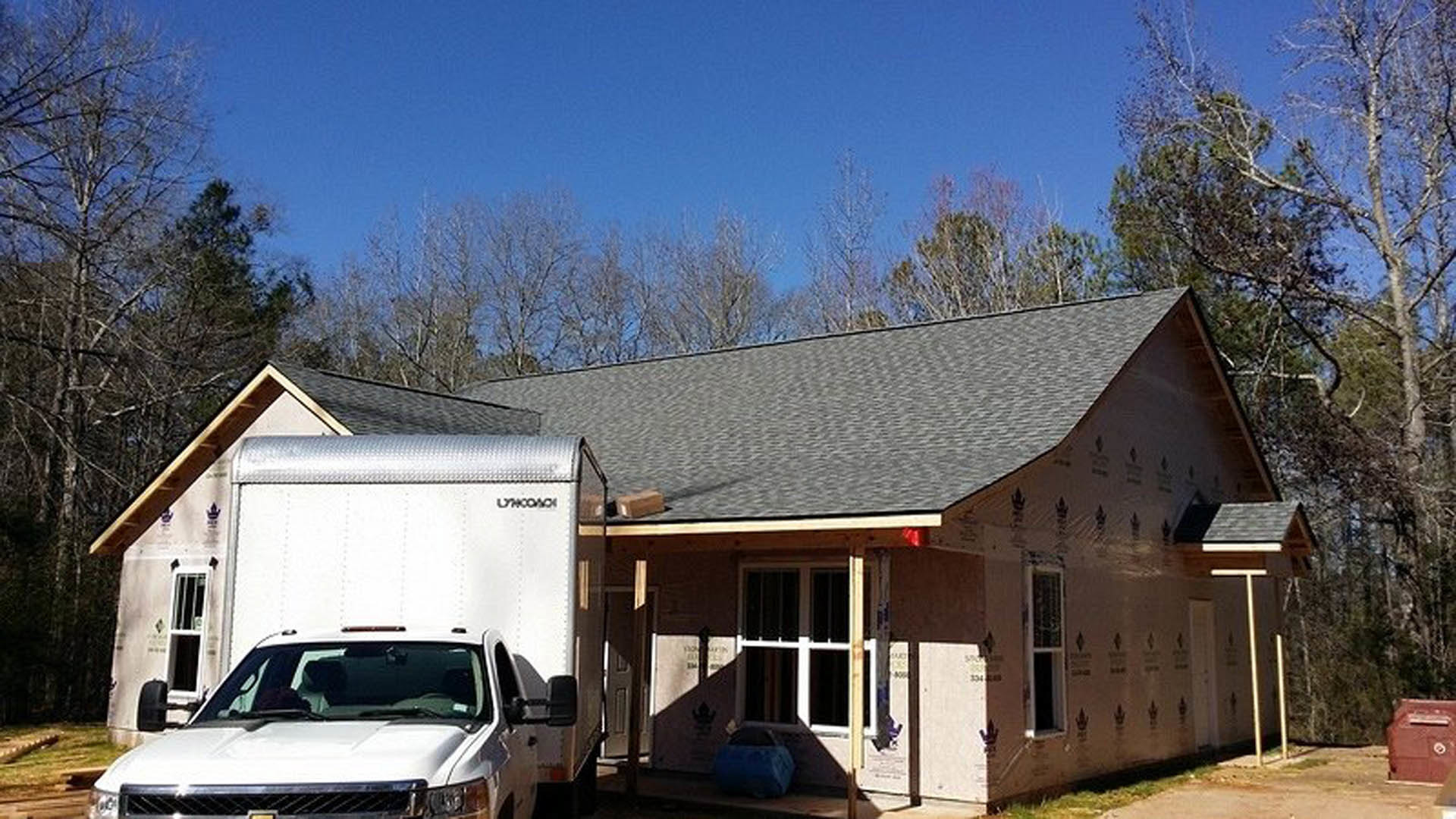 White pickup truck parked in driveway in front of a white house with large windows and a tree nearby; blue car visible in background.