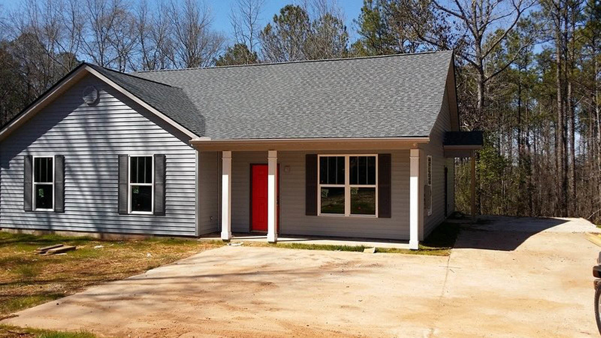 White cottage-style home with horizontal siding, prominent red front door, white-framed windows, and mature trees surrounding the property