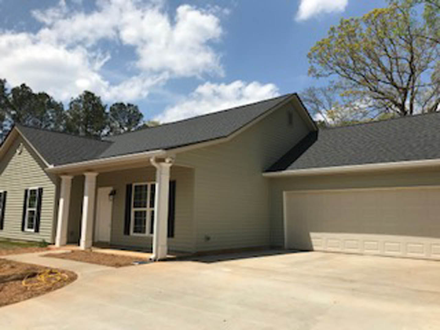 Two-story home with white siding, prominent white columns on the porch, large windows with white frames, concrete driveway, mature trees with green leaves, and blue sky with