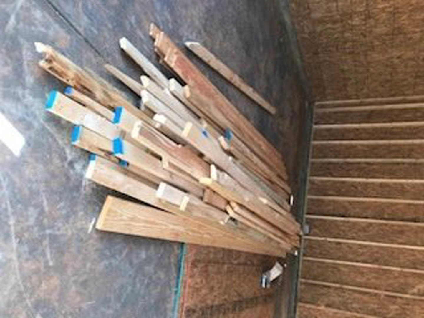 Stacked wood planks with visible grain and rough edges, set outdoors beneath an overcast sky