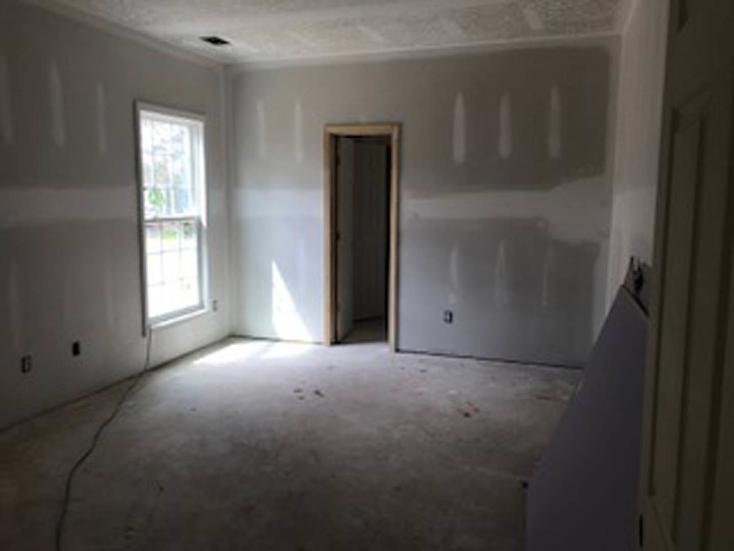 Neutral-toned room with smooth plaster walls, white-framed window, and solid door; light-colored flooring and minimal fixtures visible.