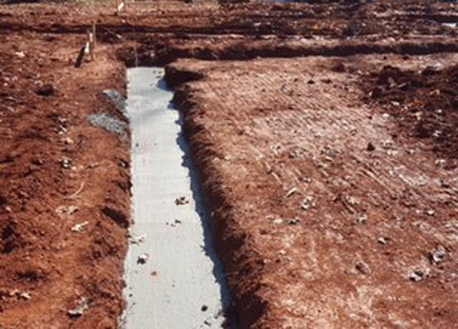 Freshly dug trench in brown soil outside, rough dirt edges visible