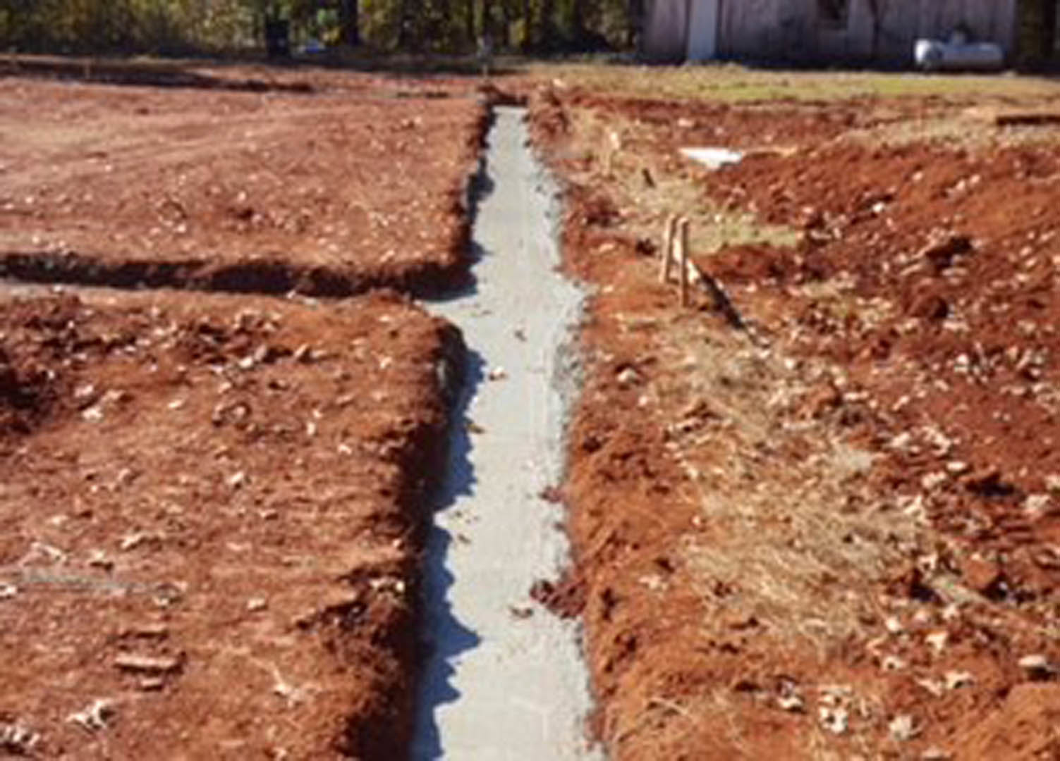 Wide trench dug in a dirt field with loose soil and sparse vegetation