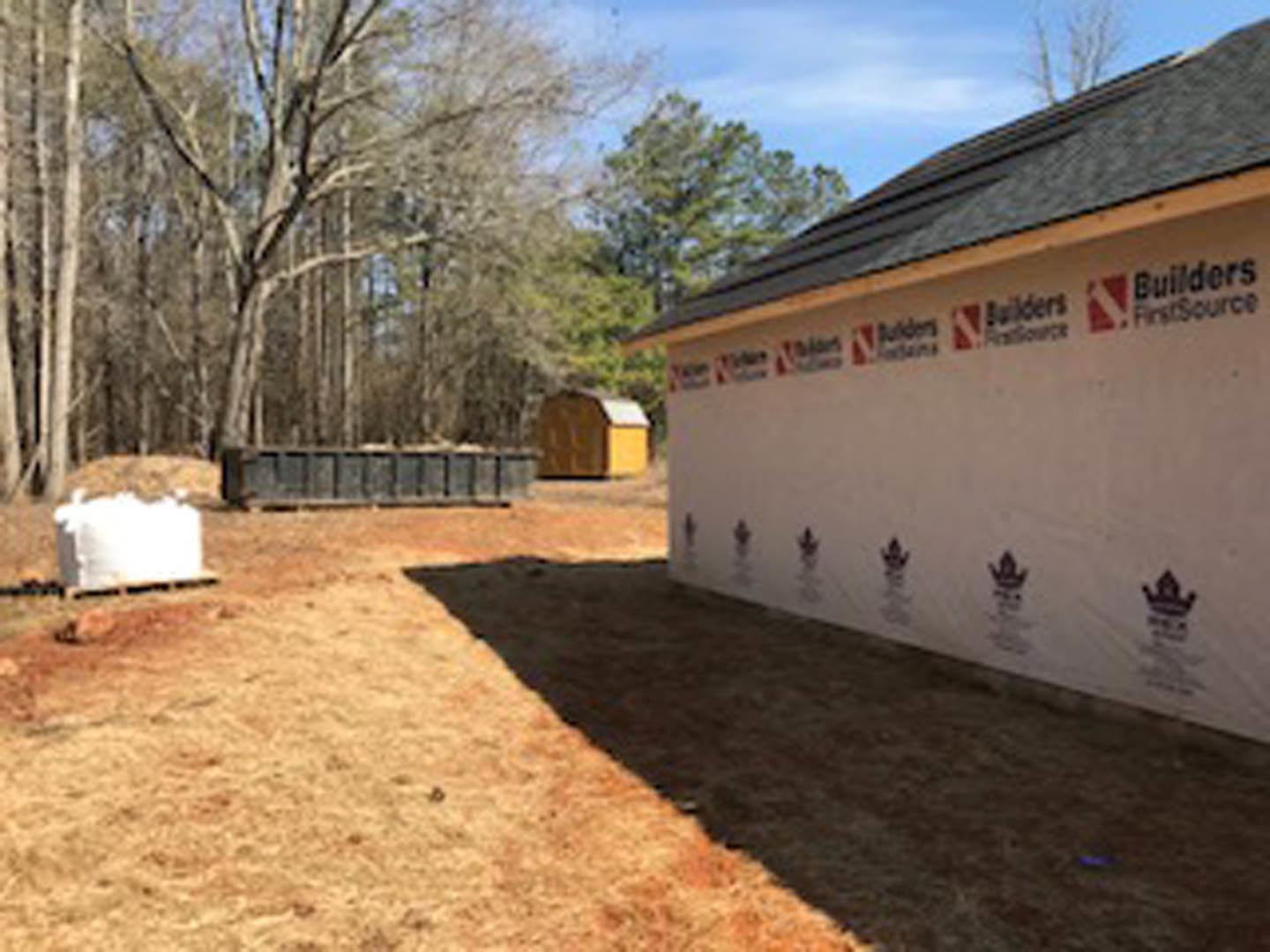 White modern house with flat roof, adjacent shed, light stucco walls, black trim, landscaped yard, cloudy sky, and mature trees in background