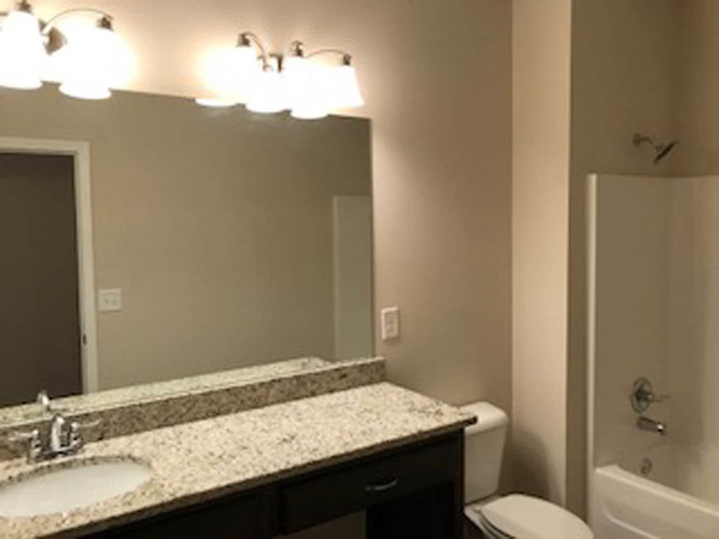 Modern bathroom featuring a rectangular mirror above a white sink with chrome faucet, white toilet with closed lid, tiled walls, and white electrical outlet.
