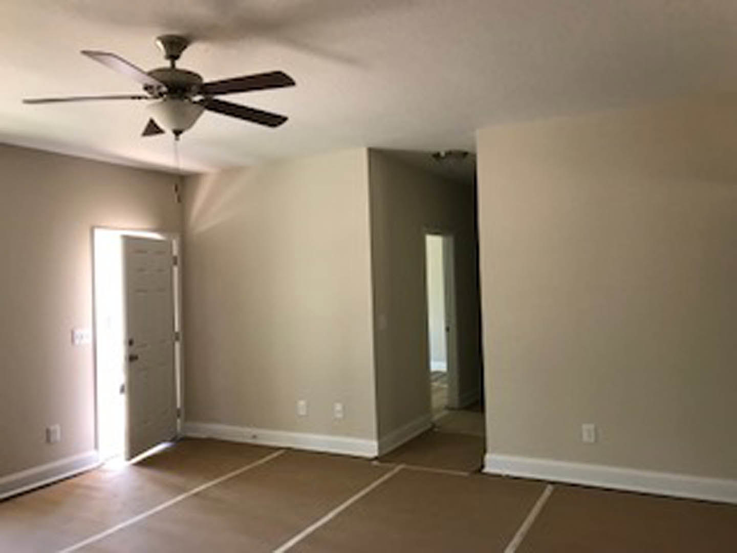 Ceiling fan with light fixture mounted on white plaster ceiling, brown laminate flooring, white door with silver handle, white light switch on wall.