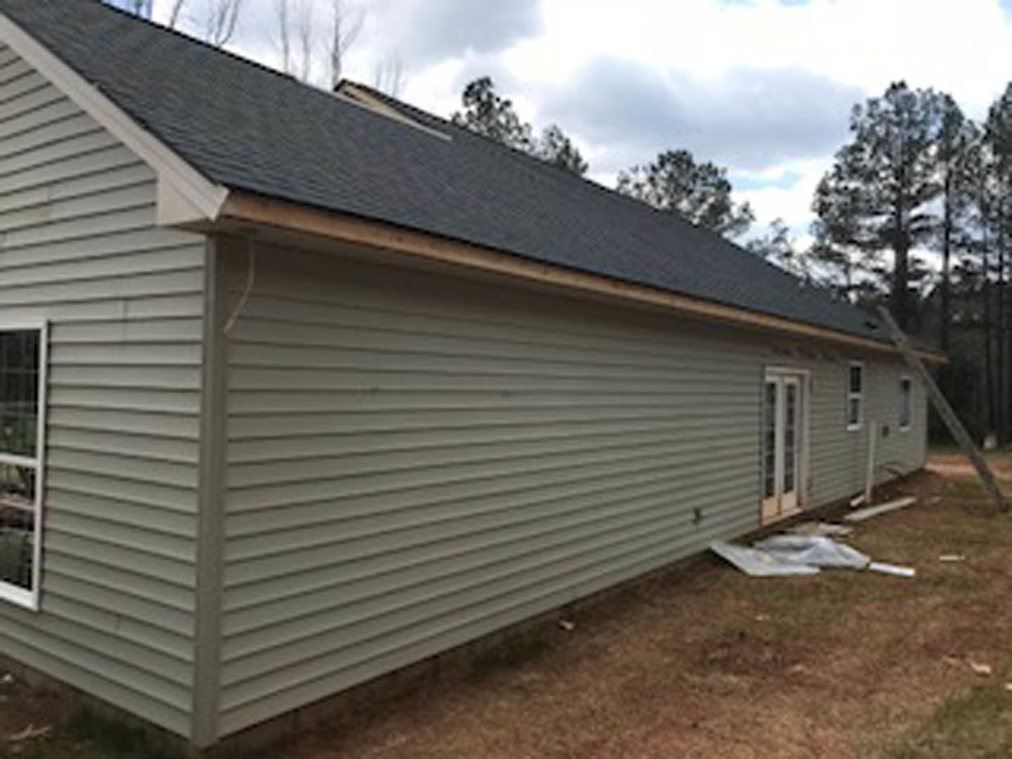 Modern home with black roof, light siding, front yard, and mature tree; ladder leaning against exterior wall