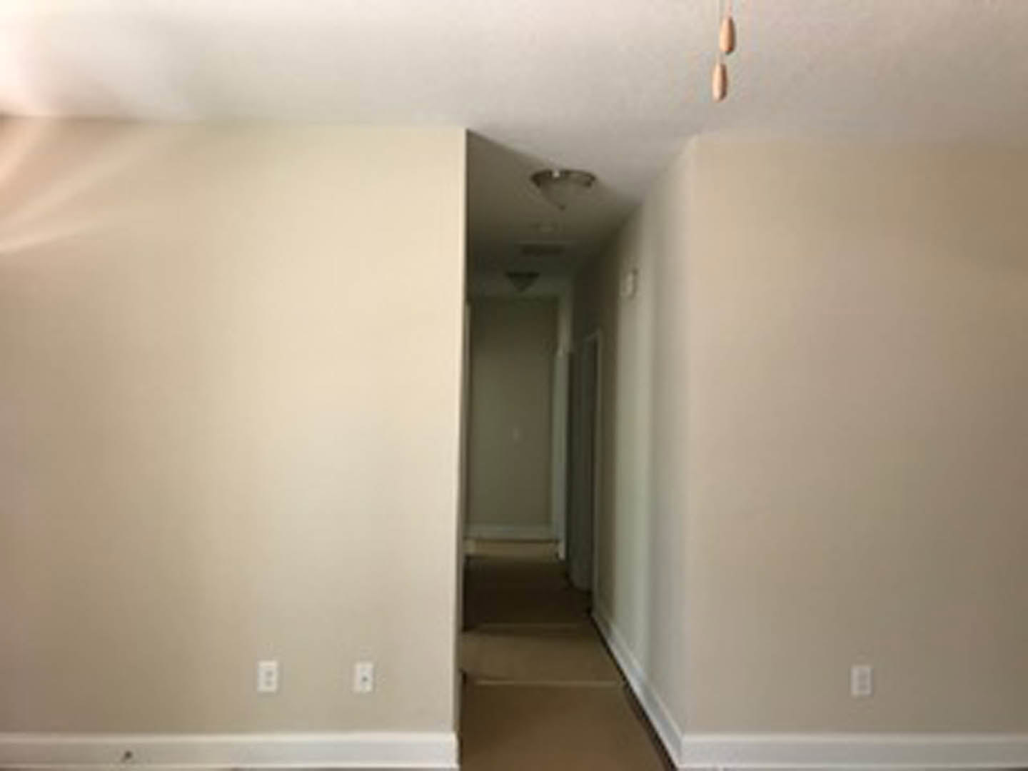 Hallway with white plaster walls, contrasting black and white trim, recessed ceiling light fixture, white electrical outlet and light switch, light wood flooring, and doorway