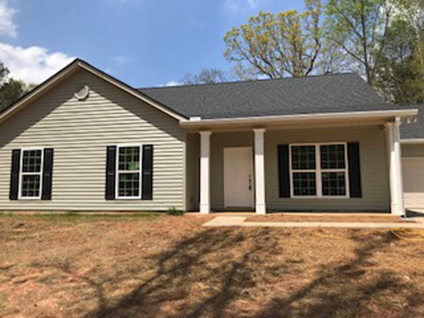 Two-story house with white columns, white-framed windows, and white front door, surrounded by green grass yard and mature trees under partly cloudy sky