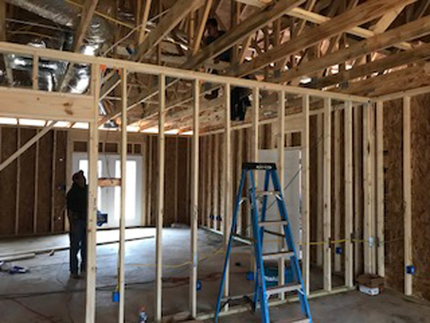 Man standing in unfinished room with exposed wooden beams, insulation, and ladder