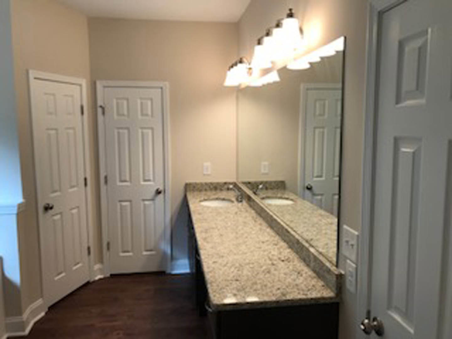 Bathroom with double vanity featuring two undermount sinks, wide framed mirror above, white walls, dark cabinetry, and tiled floor