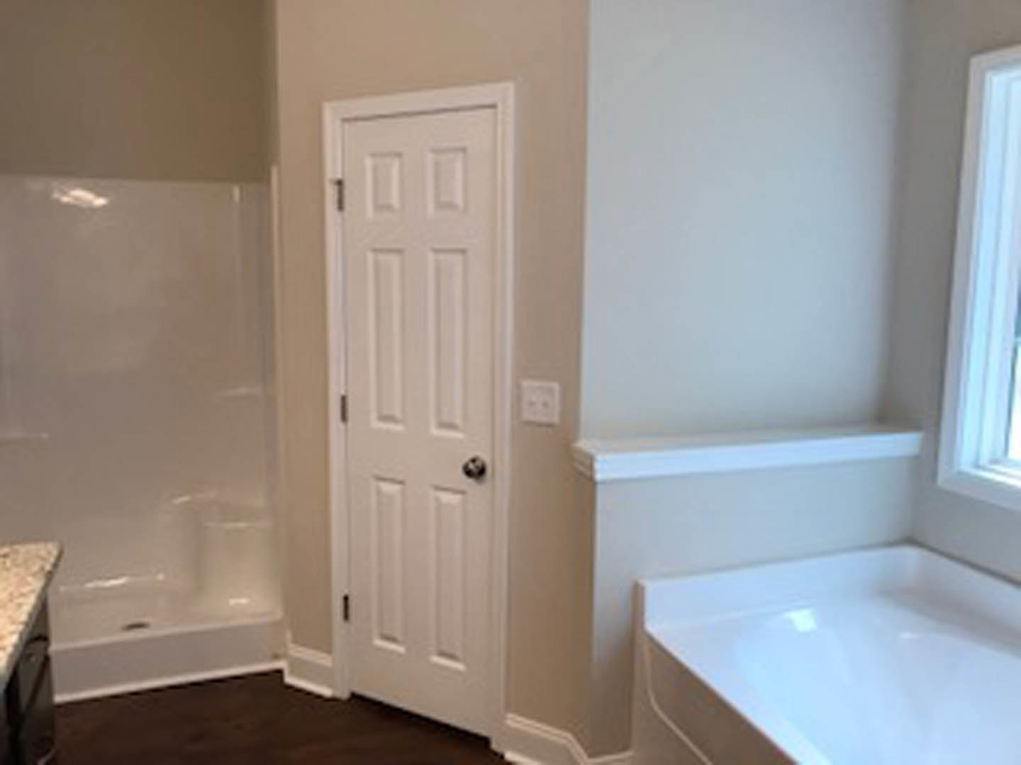 Modern bathroom featuring a freestanding white bathtub, white paneled door with chrome handle, light plaster walls, and a white wall switch.