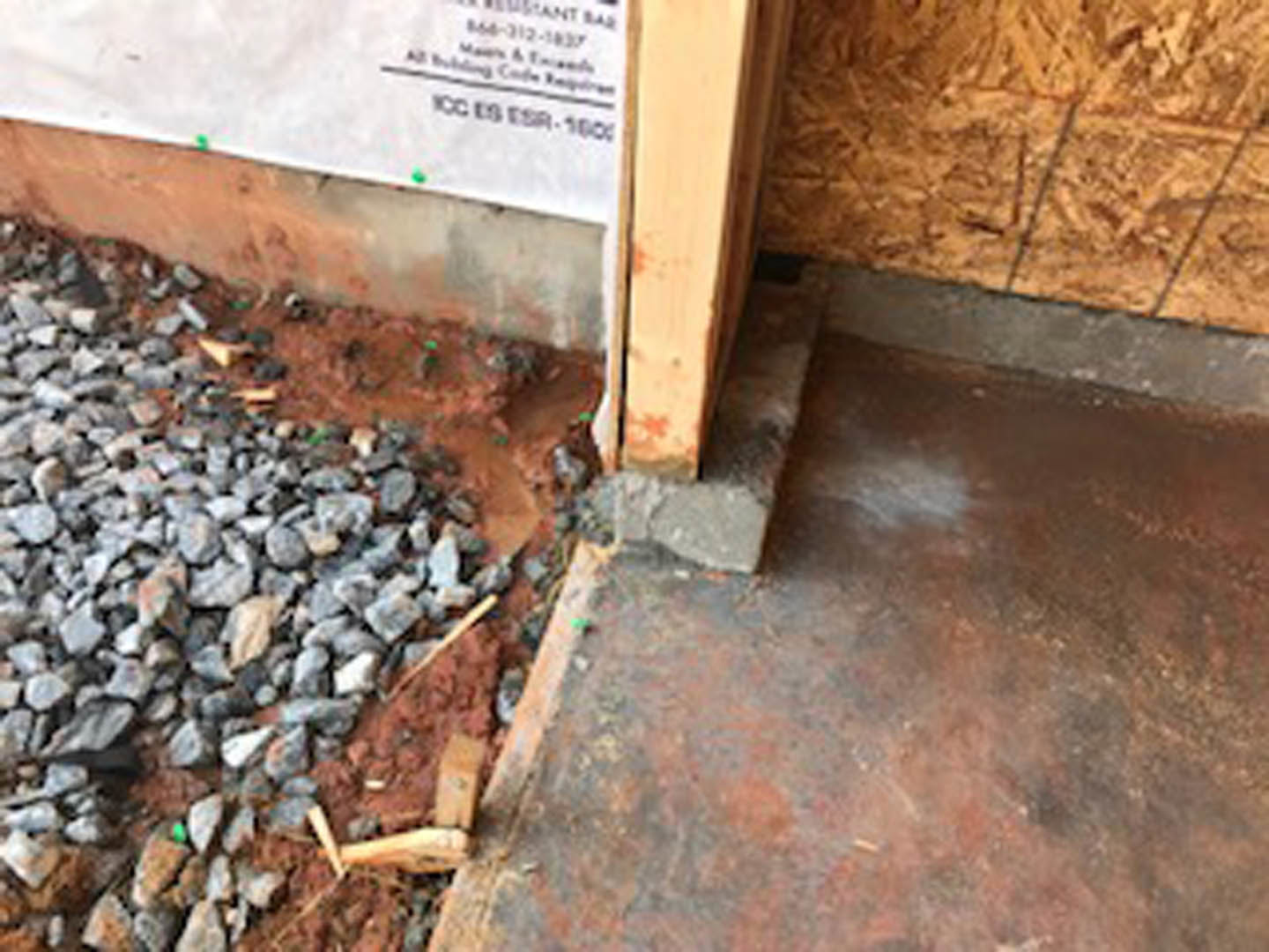Pile of rocks on bare ground beside a white sign and wood-paneled wall