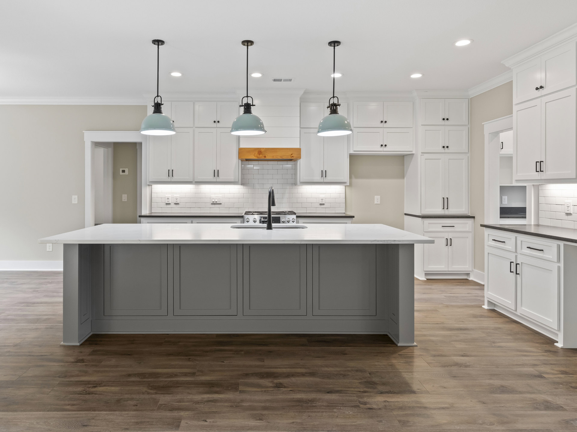 White kitchen cabinets, large central island with built-in sink and black faucet, pendant light fixture above, grey tile backsplash, light countertops, wood flooring