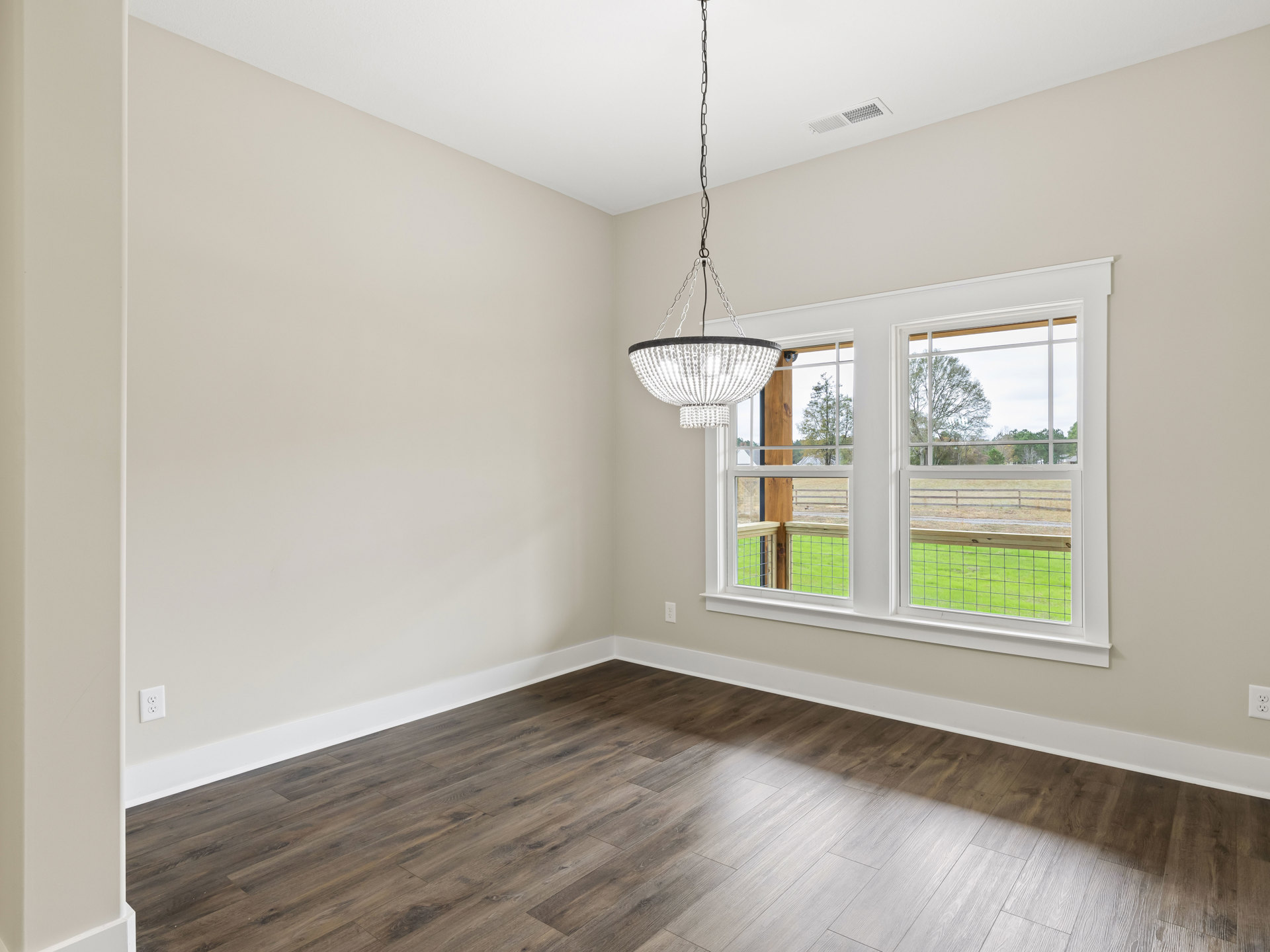Chandelier with white beaded accents hanging from ceiling, wood flooring with white trim, large windows framed by white walls