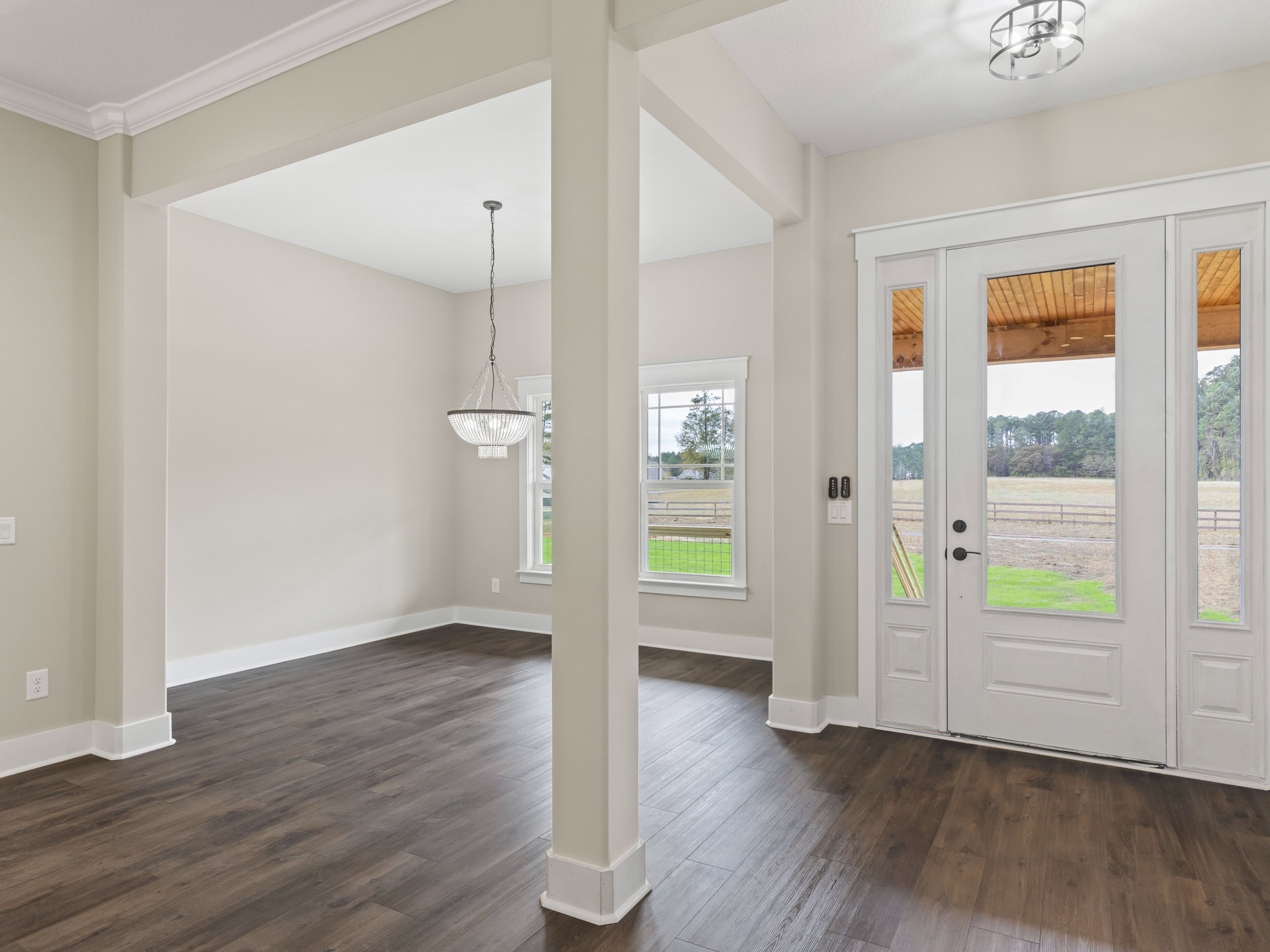 White room with wood flooring, white columns, double glass doors, single solid door, ceiling chain, and three-light fixture.