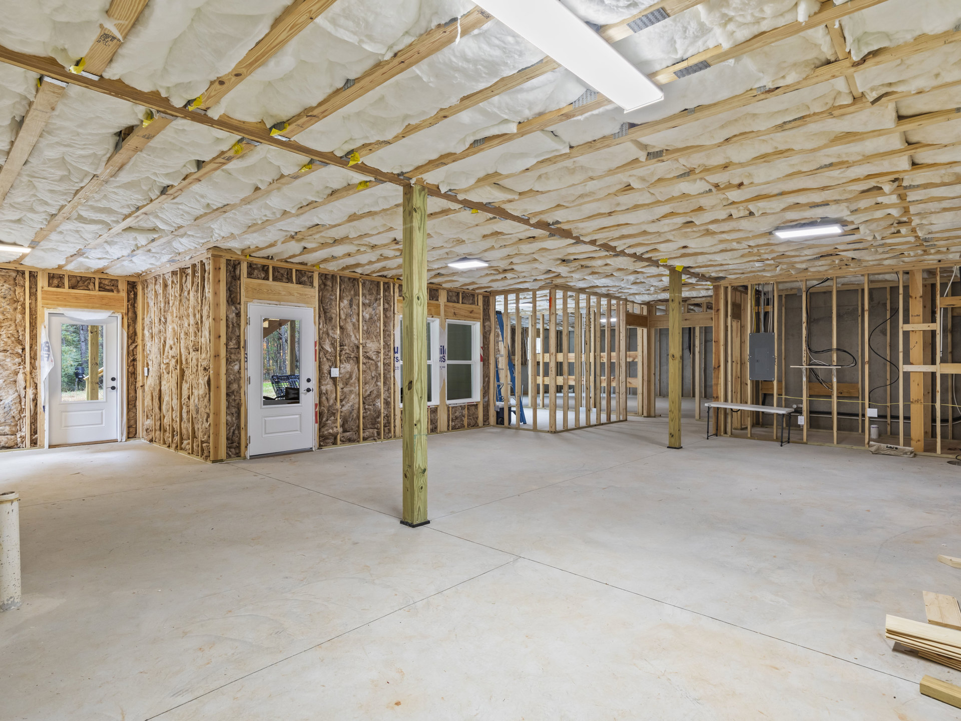 White floor with exposed wooden ceiling beams, white walls, and a white door leading outside; concrete floor section with wooden post, curtain visible in foreground.