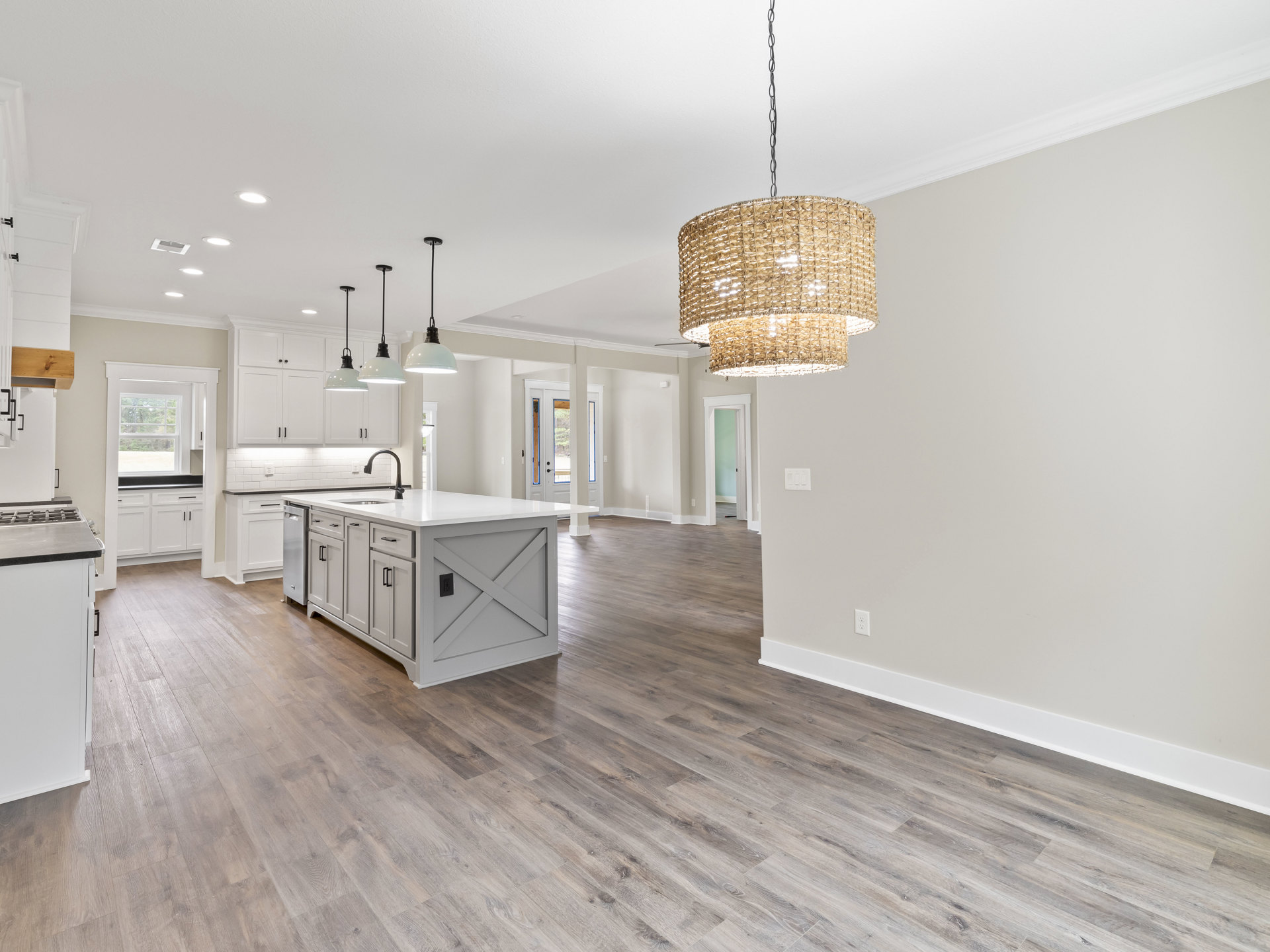 Open kitchen and dining area with wood flooring, white island featuring a sink, white cabinets with black handles, pendant light hanging from a chain, woven basket light fixture
