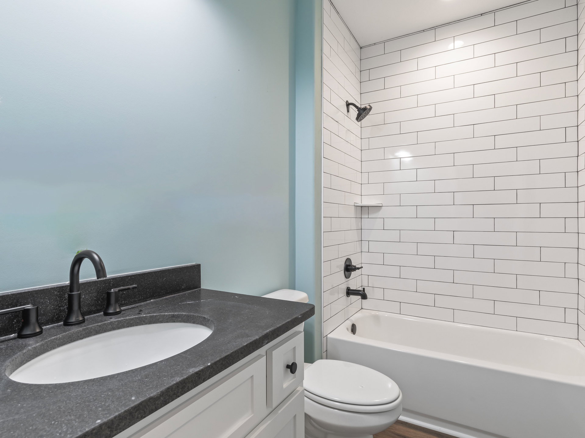 Bathroom with white tile walls, white sink and faucet, closed white toilet, black shower knob, and white bathtub adjacent to toilet