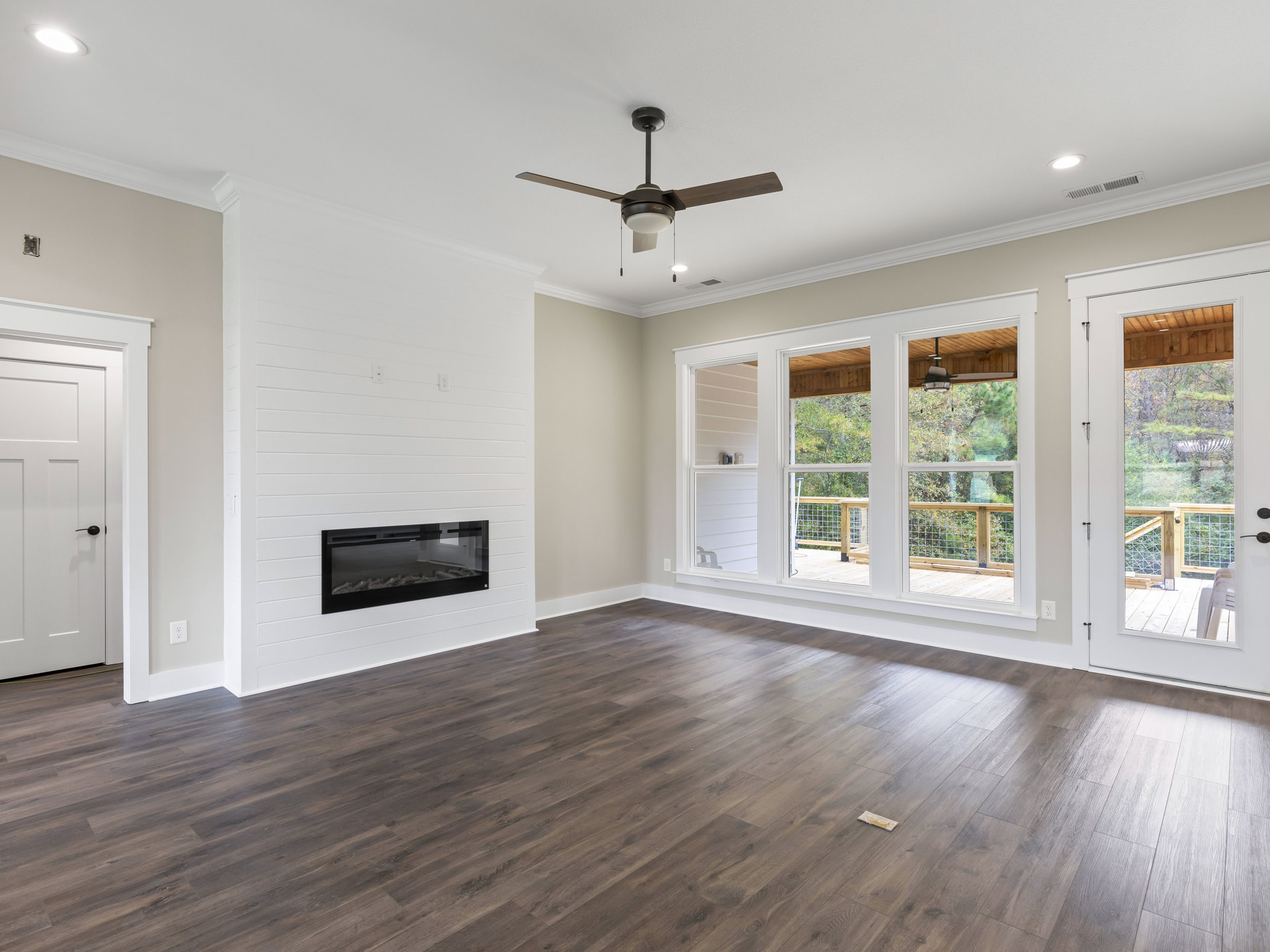 Living room with white and black fireplace, wood flooring, ceiling fan, and white door with black handle