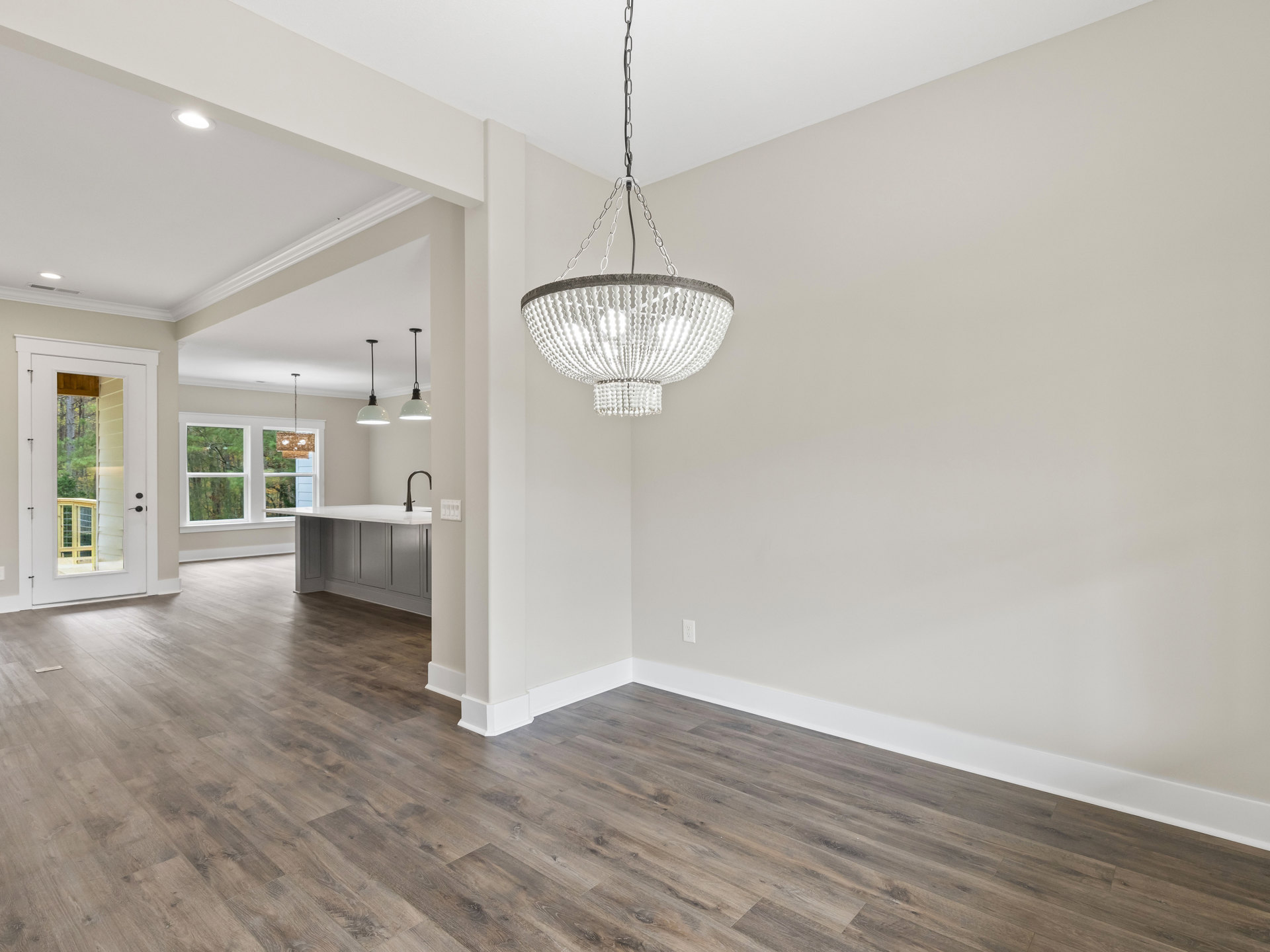 White beaded chandelier hanging from plaster ceiling, wood flooring, white walls, door with window overlooking trees