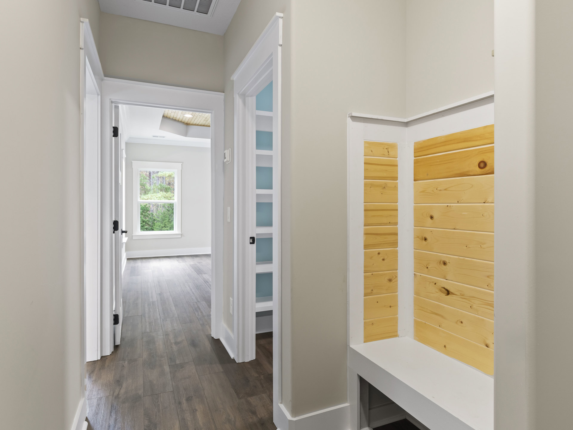 Hallway with wood flooring, wood paneled wall, large window showing trees outside, white trim, and yellow accent wall