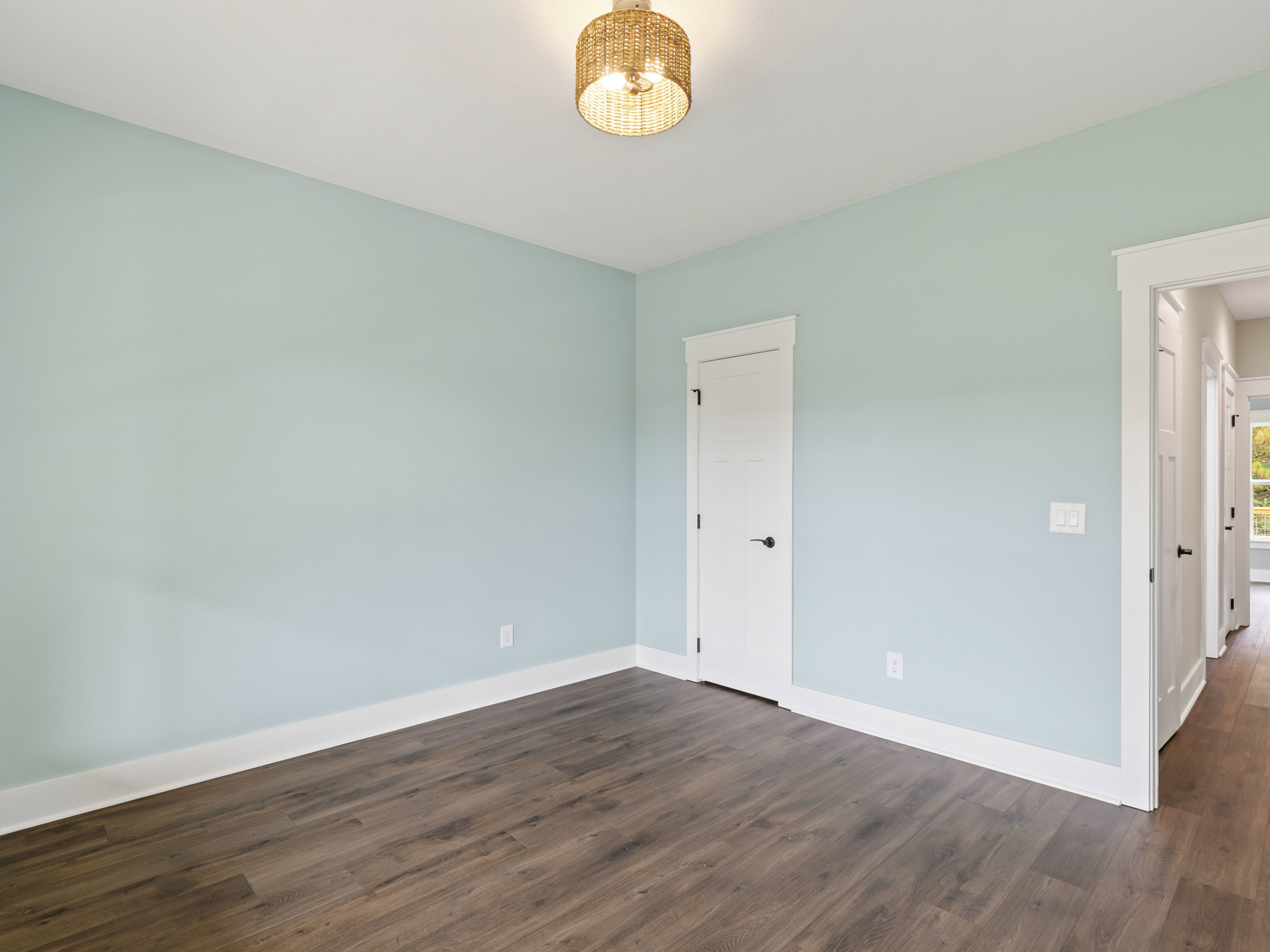 Woven pendant light hangs above wood laminate flooring, white door with black handle, white walls with plaster molding