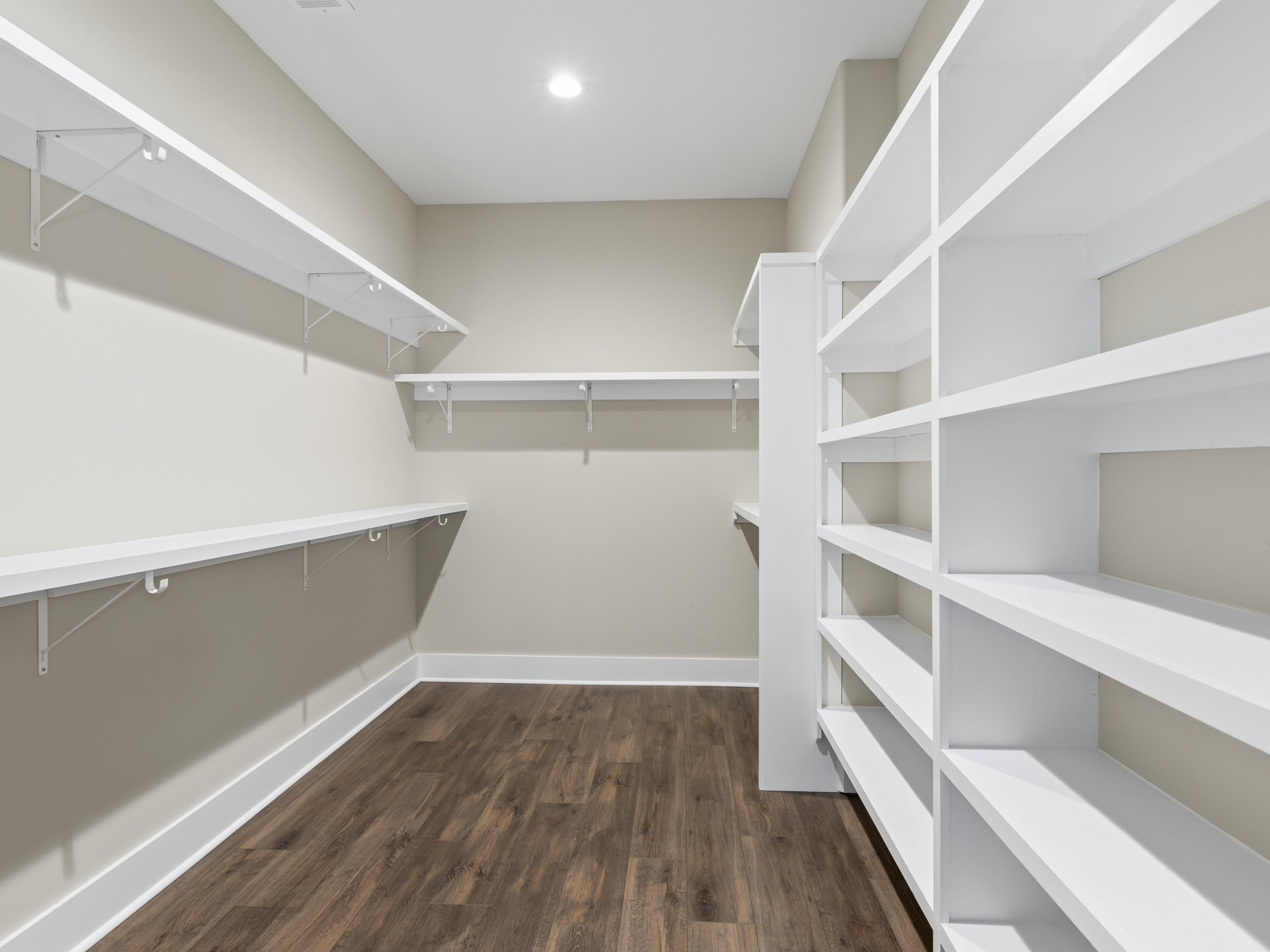 Empty walk-in closet with white built-in shelves, wood flooring with white trim, and a ceiling light fixture