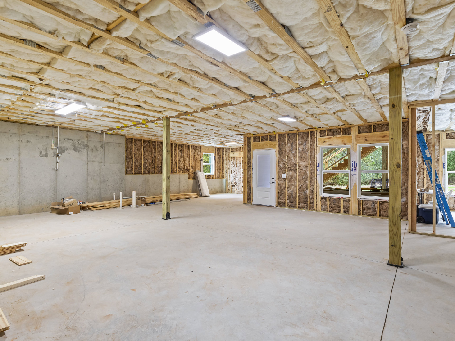 White ceiling with recessed light, pale walls, white door with black handle, blue ladder near window, plastic crate on floor