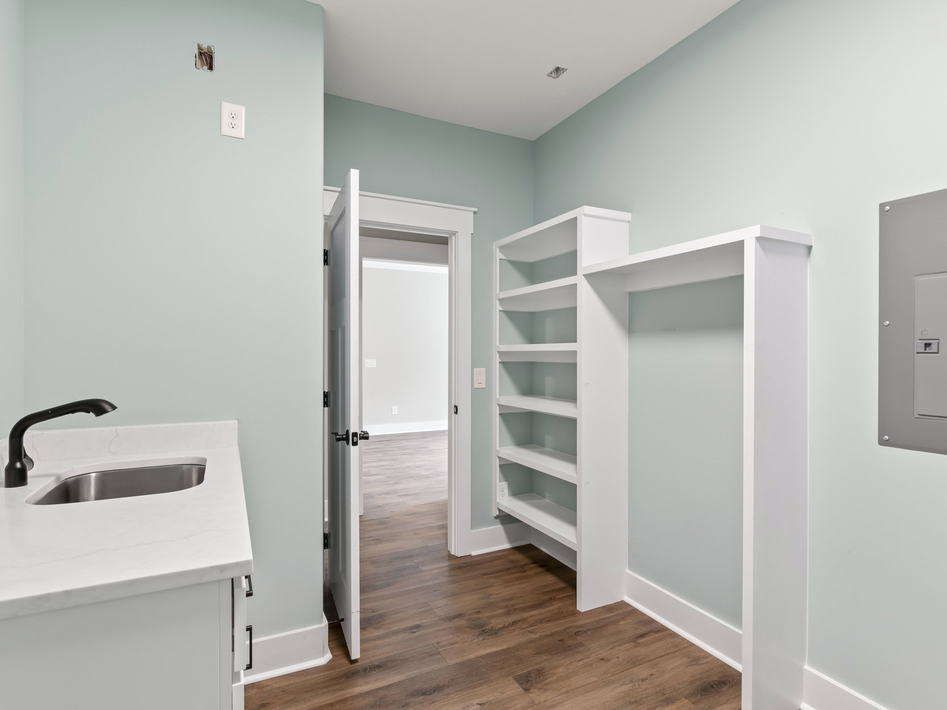 White built-in shelves and cabinetry, white countertop with black faucet and sink, light wood flooring, open door leading into the room