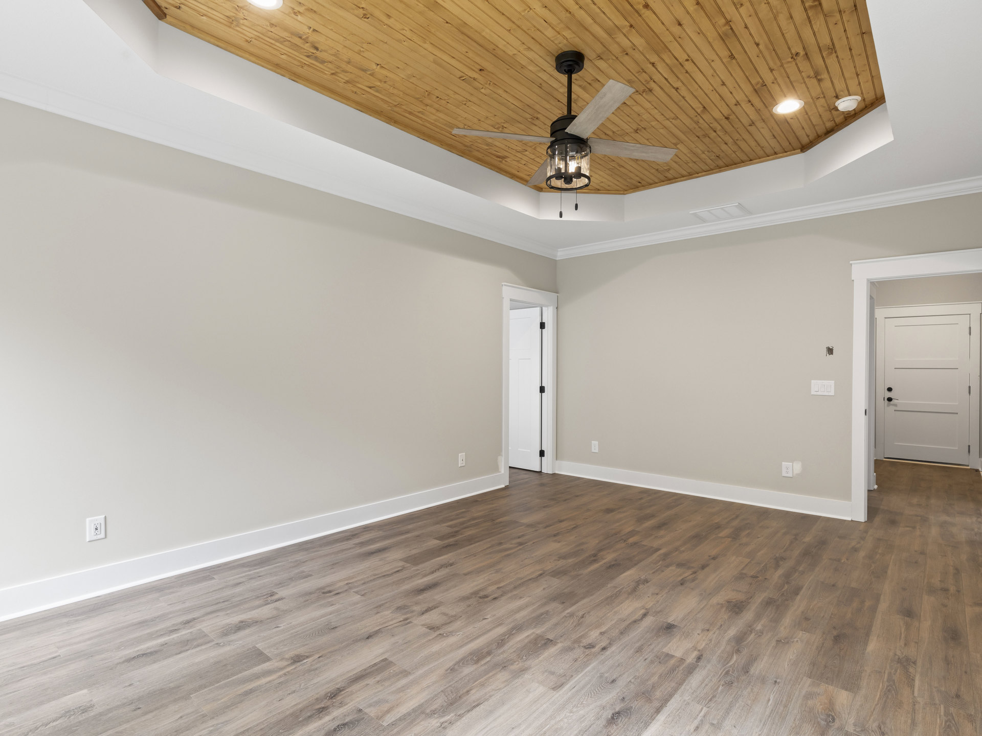 Ceiling fan with glass light fixture, wood flooring, white walls, white door with black handle and hinge